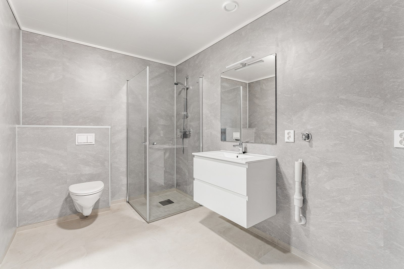 Badet er utstyrt med vegghengt toalett, dusj med glassdører og servant med moderne innredning. Det er opplegg for vaskemaskin. Galleribilde