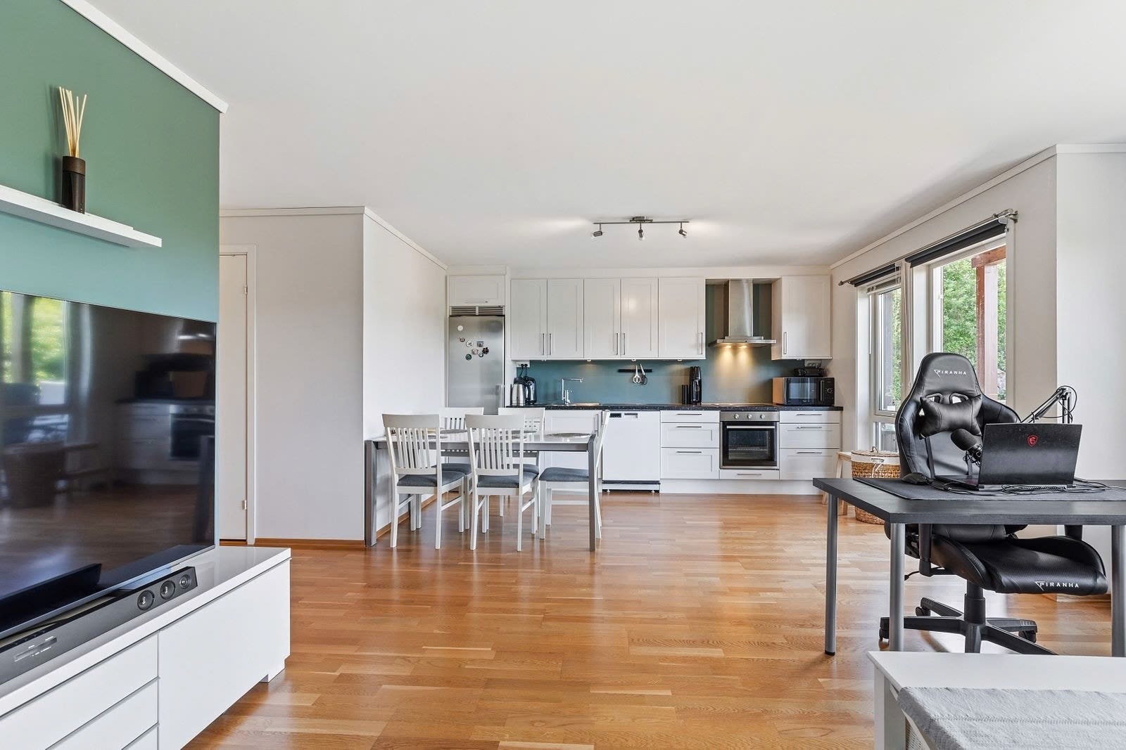 Ett romslig kjøkken med grå benkeplate og hvite skapdører, god benke- og skapplass med hvitevarer. Galleribilde