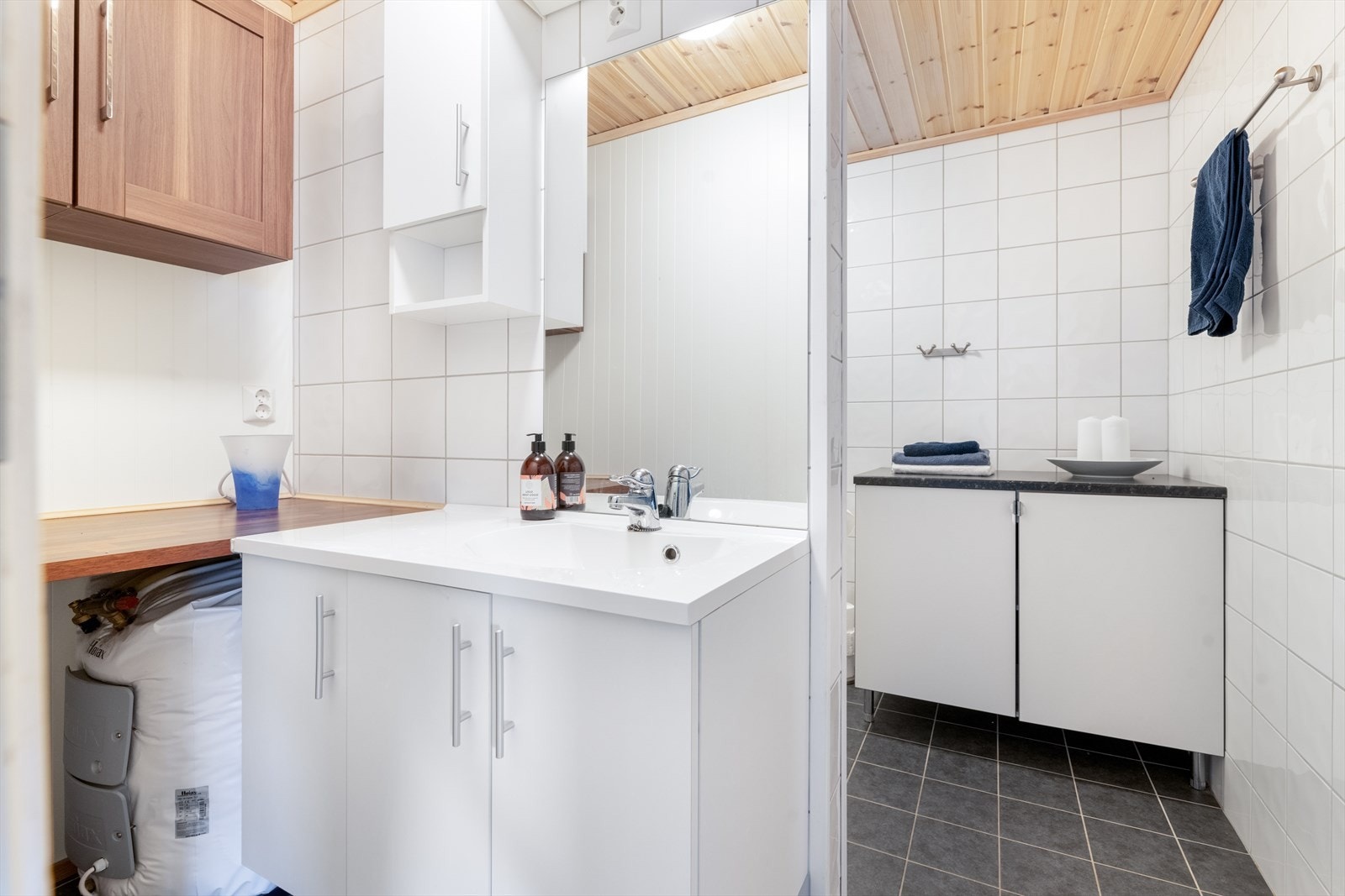 Helfliset bad med varmekabler i gulv. Badet er innredet med toalett, dusjhjørne og servantinnredning med underskap, overskap og speil. Galleribilde