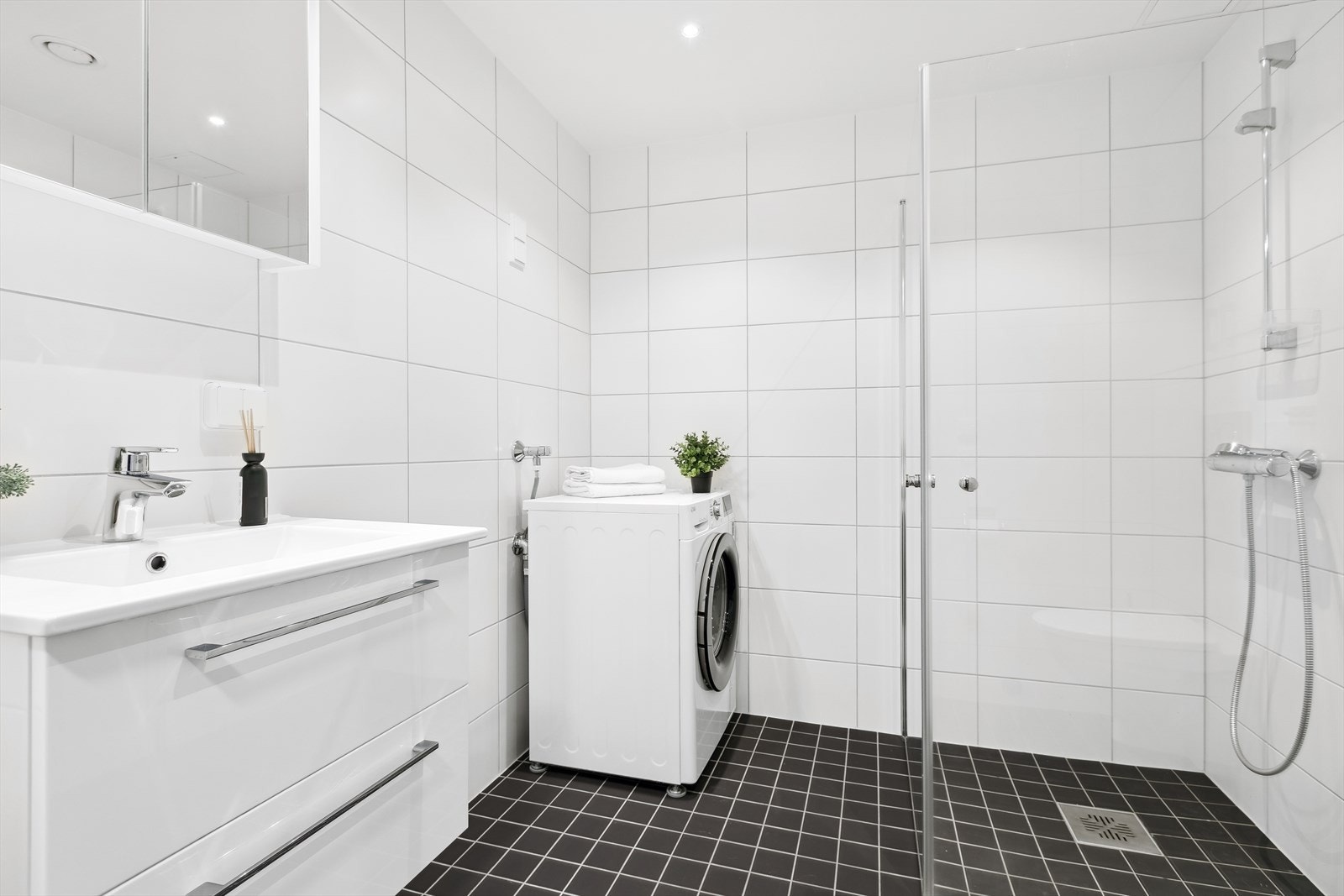 Det er vegghengt toalett, opplegg for vaskemaskin og tørketrommel og et dusjhjørne med innfellbare glassdører. Galleribilde