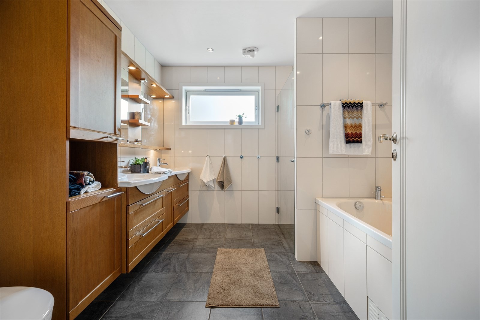 Badet i 1. etasje fremstår som moderne og praktisk, med flislagte gulv og vegger som gir et helhetlig og stilrent uttrykk. Galleribilde