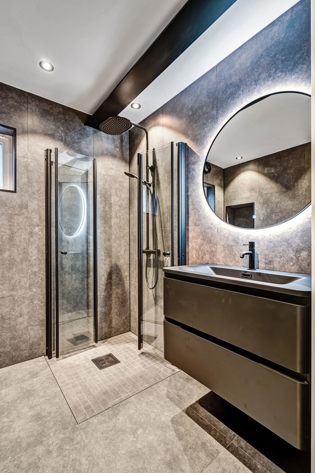 Flislagt og innbydende bad utstyrt med dusjhjørne med tropedusj, servant med underskap og baklyst speil. Galleribilde