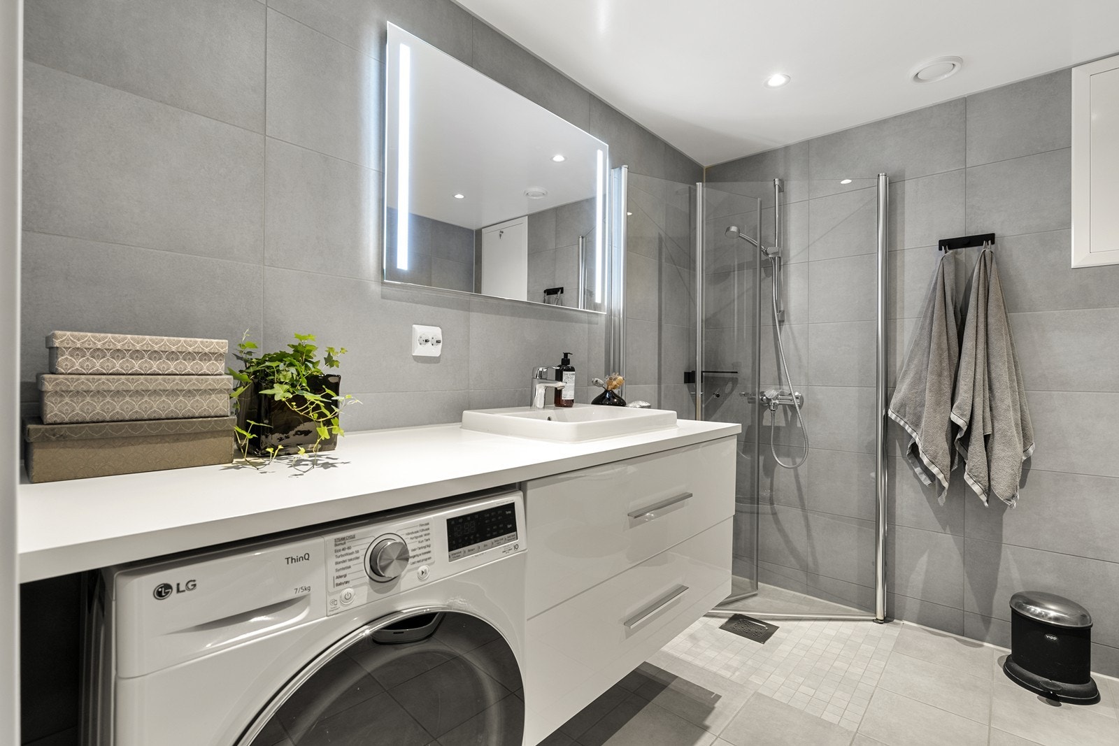 Badet har vegghengt toalett, servant med skuffer og dusjnisje med innfellbare glassdører. Kombimaskin for vask og tørk medfølger. Galleribilde