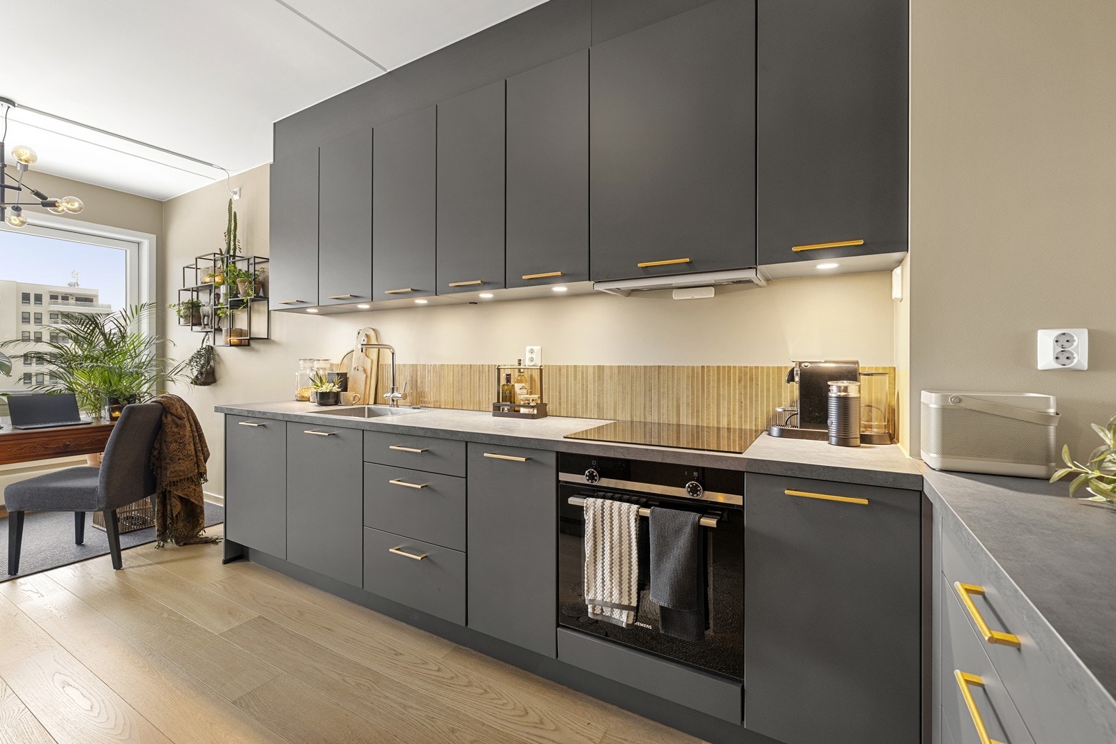 Innredning med slette, grå fronter, laminat benkeplate og belysning under overskap. Helintegrert kjøl- og fryseskap. Galleribilde