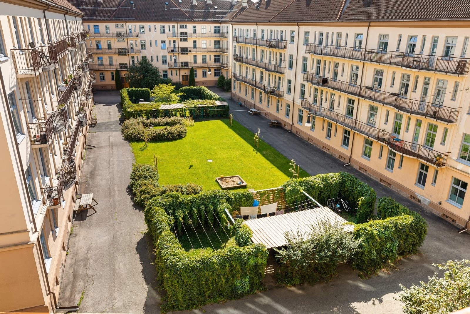 Sommer i bakgården. Pent opparbeidet bakgård med beplantning, sittegrupper og sykkelskur. Galleribilde