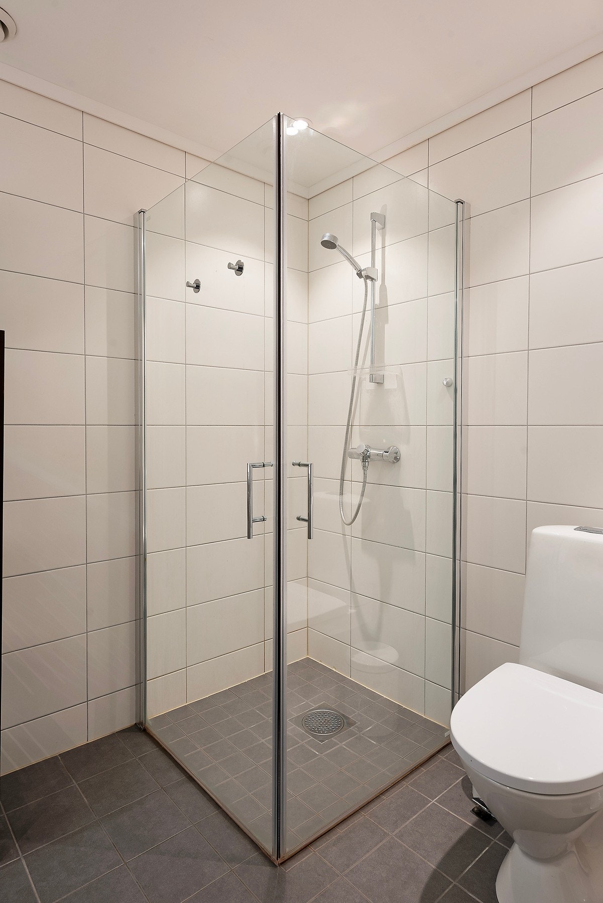 Et moderne bad med dusjhjørne med glassdører, toalett, servantinnredning og opplegg til vaskemaskin Galleribilde