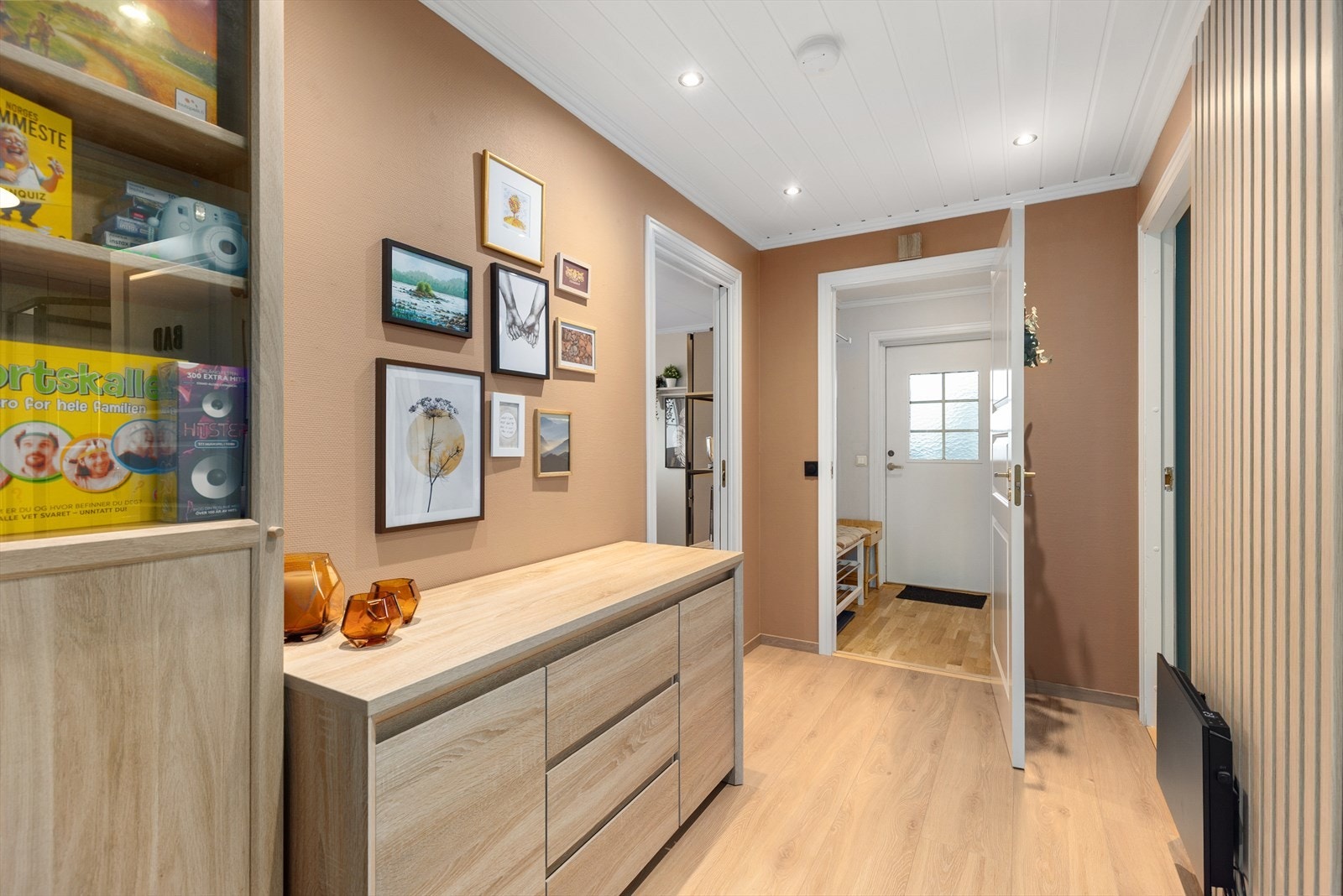 Videre inn er det en mellomgang, med nytt laminatgulv og ny spilevegg som tilfører både dybde, varme og kontrast. Gangen har plass til mindre møblering, og det er down-light belysning i tak. Galleribilde