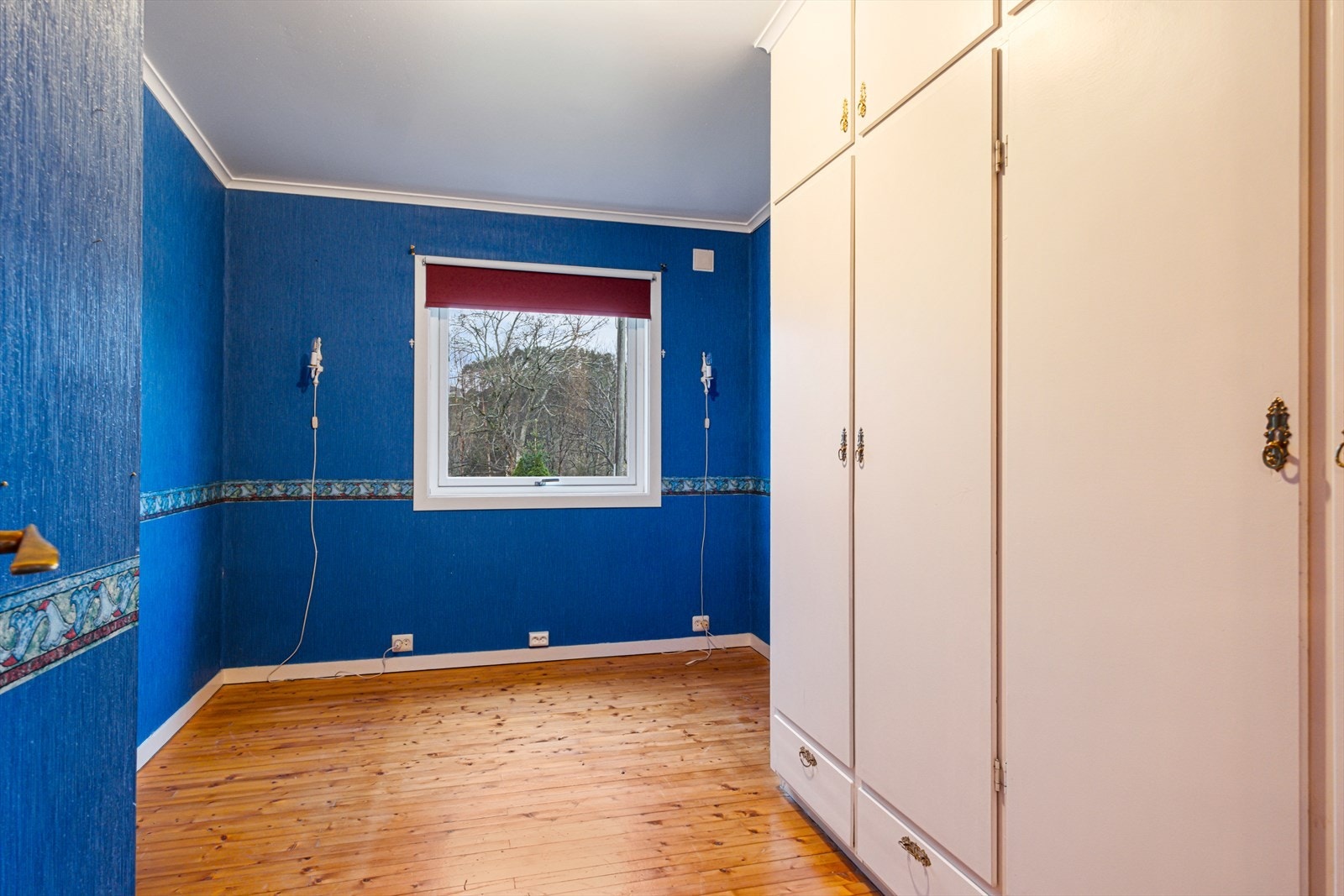 Rommet har tregulv og tapetserte vegger, samt et vindu Galleribilde