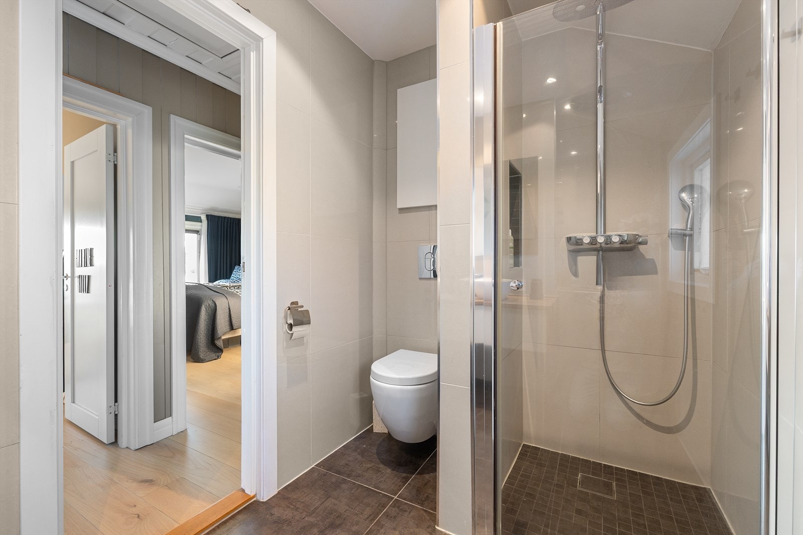 Badet er utstyrt med dusjhjørne med innfellbare glassdører, veggmontert toalett og bred baderomsinnredning med skuff, heltre eikebenk, servantbolle med ettgrepsarmatur fra Grohe og vegghengt speil. Galleribilde