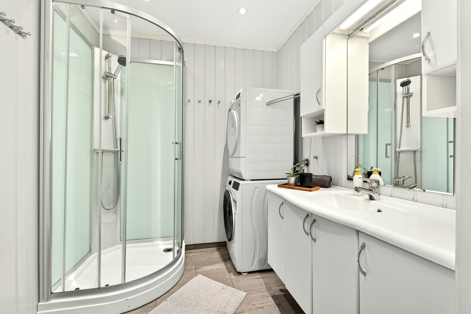 Badet har fliser på gulv med behagelig gulvvarme, dusjkabinett, innredning med skapløsning, speil med sideskap, og opplegg for vaskemaskin. Galleribilde