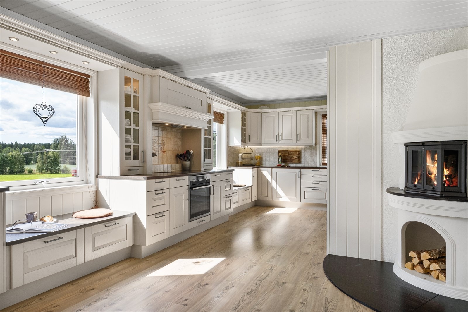 Lyst og romslig kjøkken med store vinduer som gir rikelig med naturlig lys og en koselig peis for kalde dager. Galleribilde