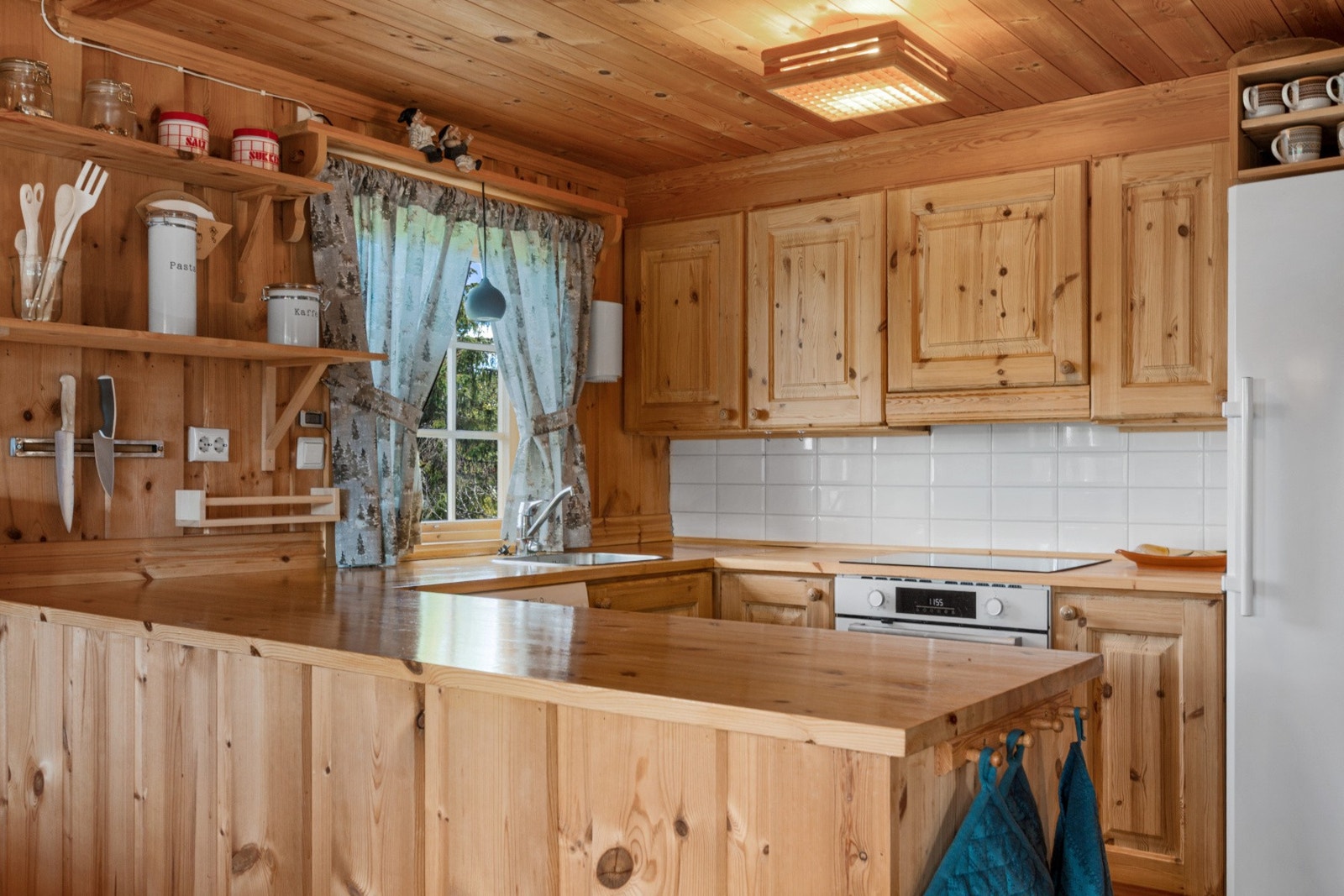 Kjøkkeninnredning i heltre med nedfelt kjøkkenkum, komfyr med platetopp, oppvaskmaskin og kjøl-/fryseskap. Galleribilde