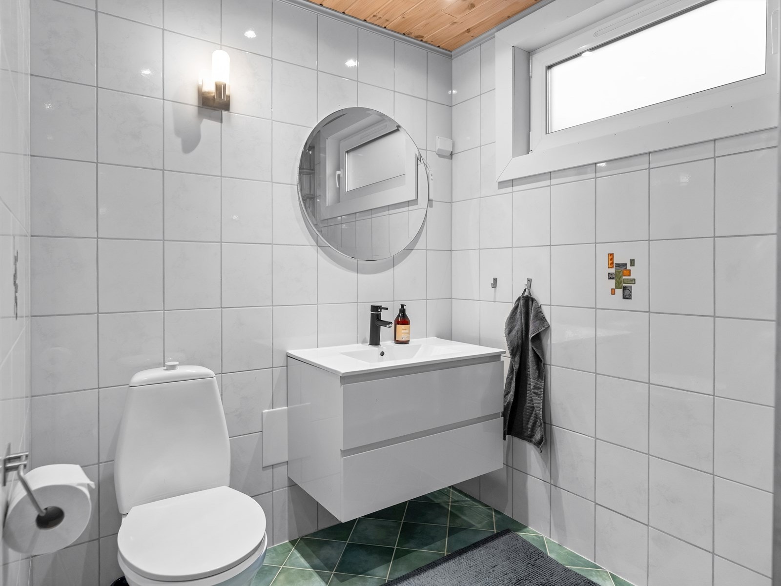 Rommet har dusj på gulv med dører i herdet glass samt gulvstående klosett. I tillegg er det montert servant med benkeskap. Galleribilde