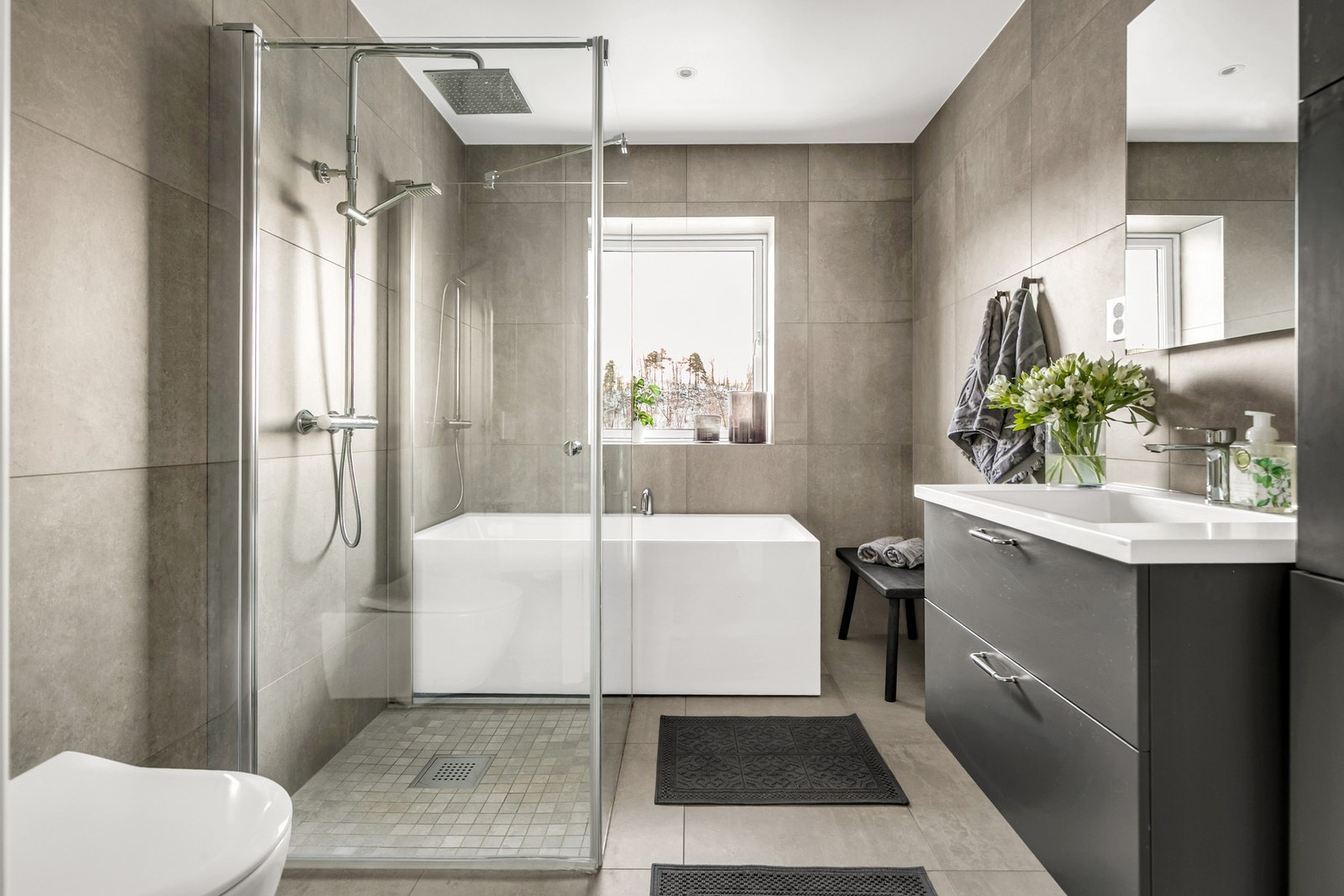 Badet er av god størrelse og rommer et badekar, vegghengt wc, servant med underskap og dusj. Et romslig og stilrent bad med tidløse materialvalg og gjennomført uttrykk. Galleribilde