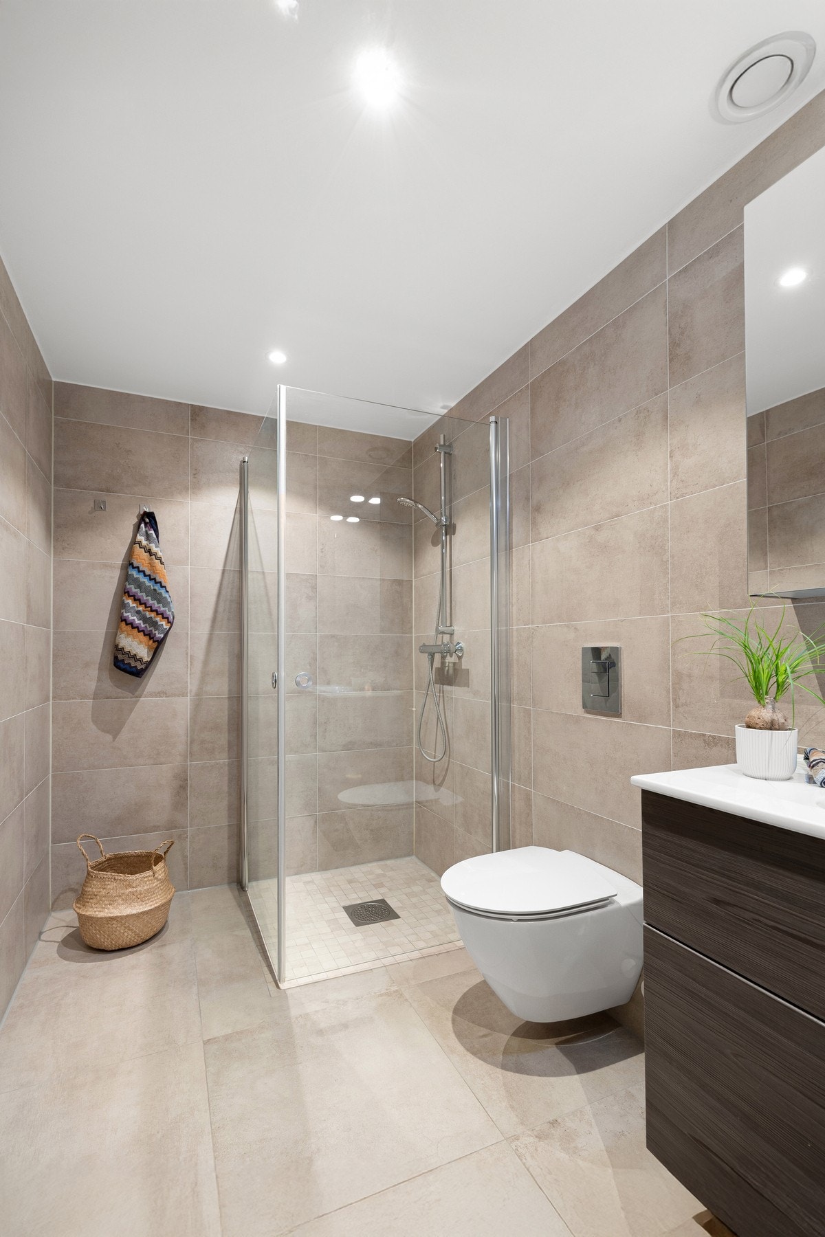 Badet er innredet med store fliser i serien Clays Shell, mosaikk i dusjsonen, vegghengt WC og moderne baderomsinnredning med speilskap. Galleribilde