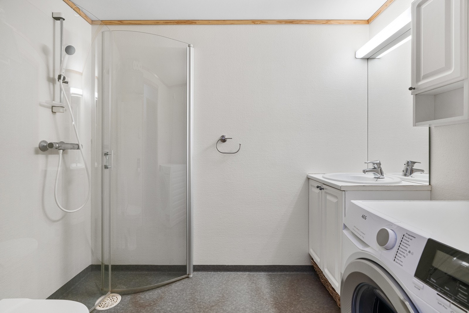 Lyst baderom med praktiske innfellbare dusjvegger. Badet er utstyrt med servant i innredning, toalett og opplegg for vaskemaskin. Galleribilde