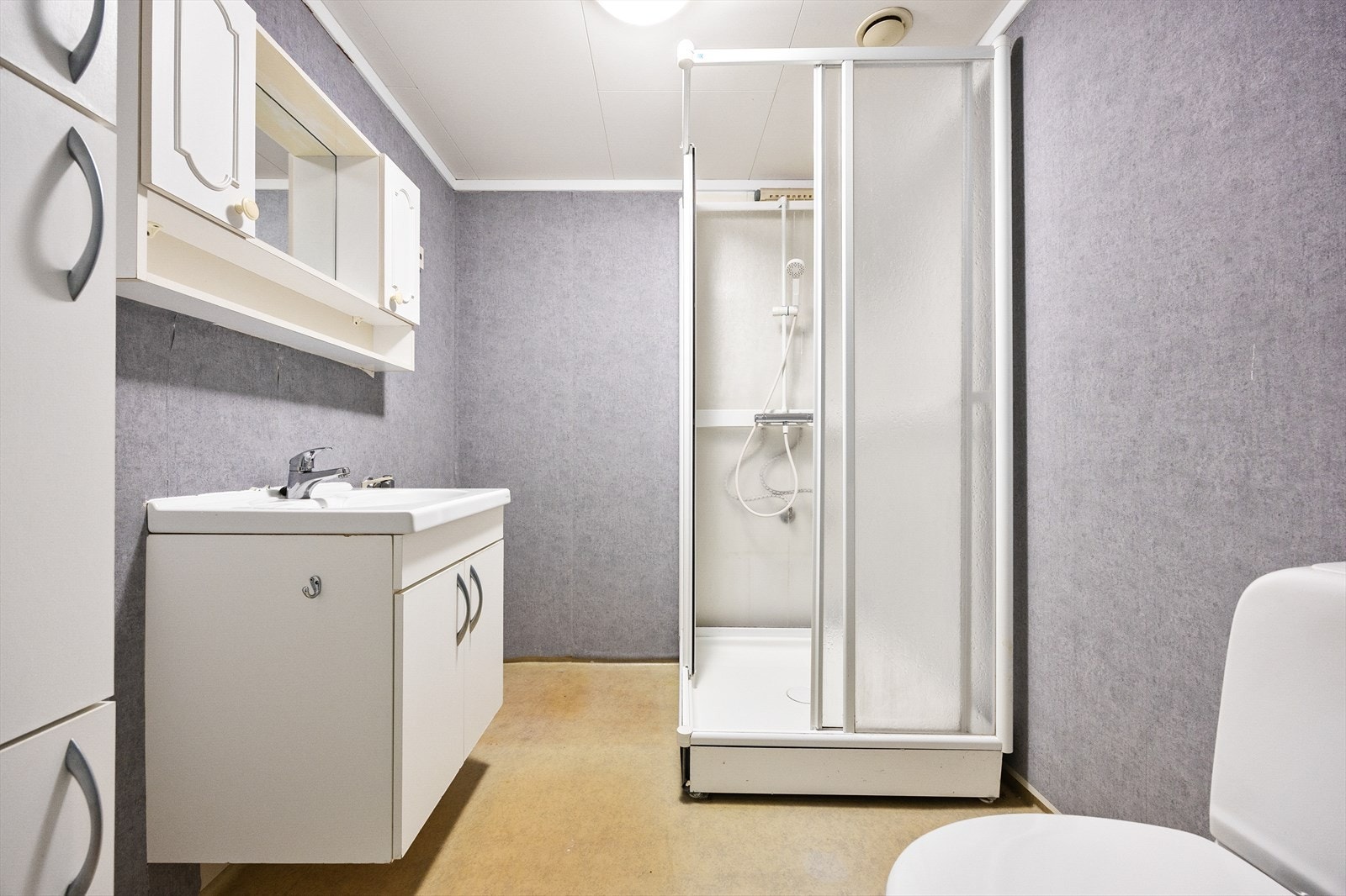 Badet har innredning med heldekkende servant over skapseksjon, matchende veggskap og speil med hyller og belysning. Galleribilde