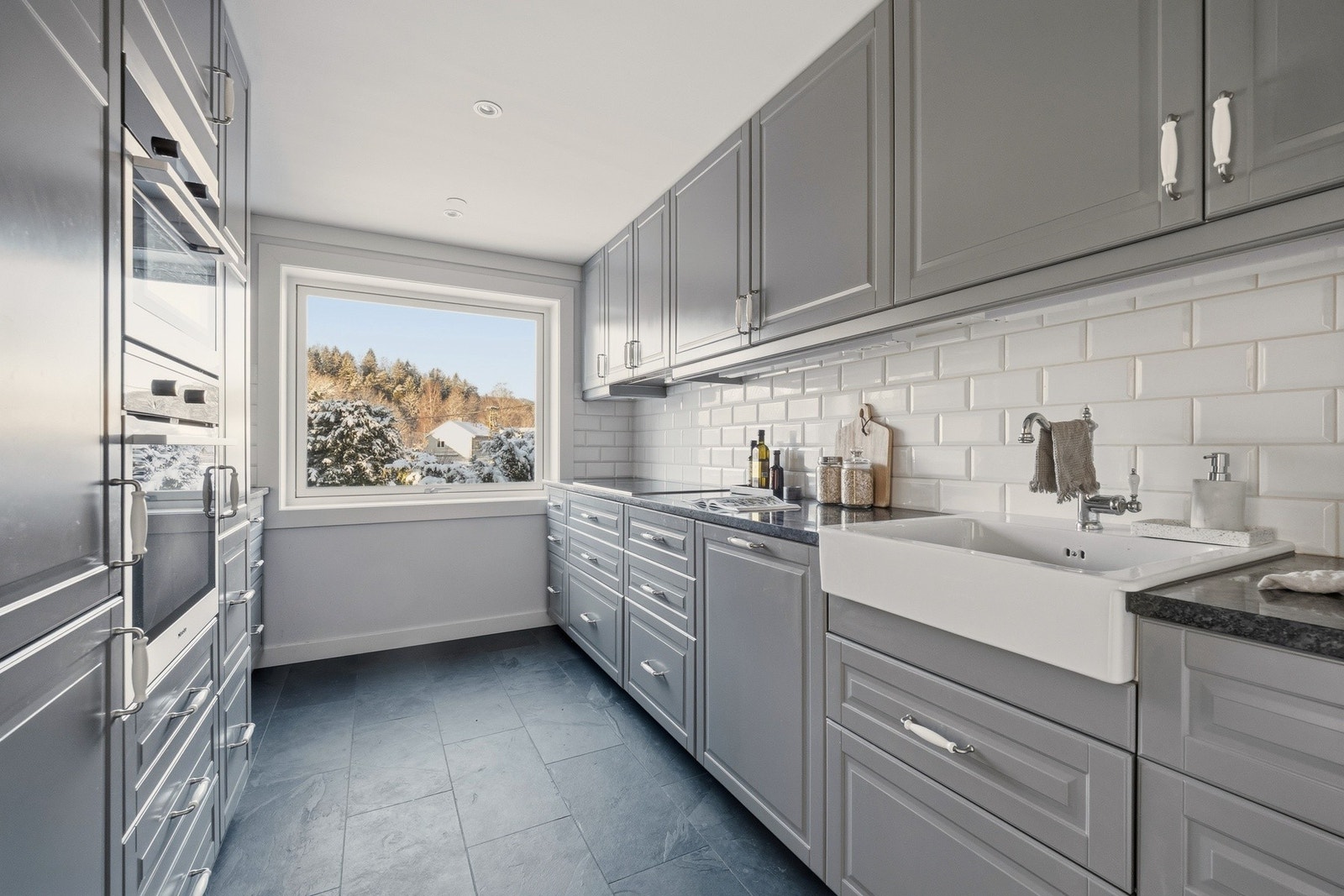 Kjøkkenet er utformet med gode materialvalg. Med profilerte fronter, stein benkeplate, og ovenpåliggende oppvaskkum, er det både stilfullt og funksjonelt. Galleribilde