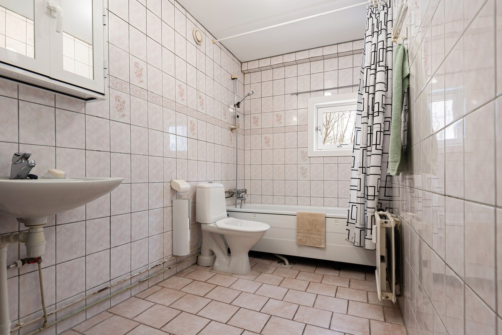 Romslig bad med innredning bestående av veggskap og høyskap, utstyrt med speil samt profilerte/glatte fronter. Badet har dusj i badekar, servant og klosett. Det er veggmontert varmeovn Galleribilde