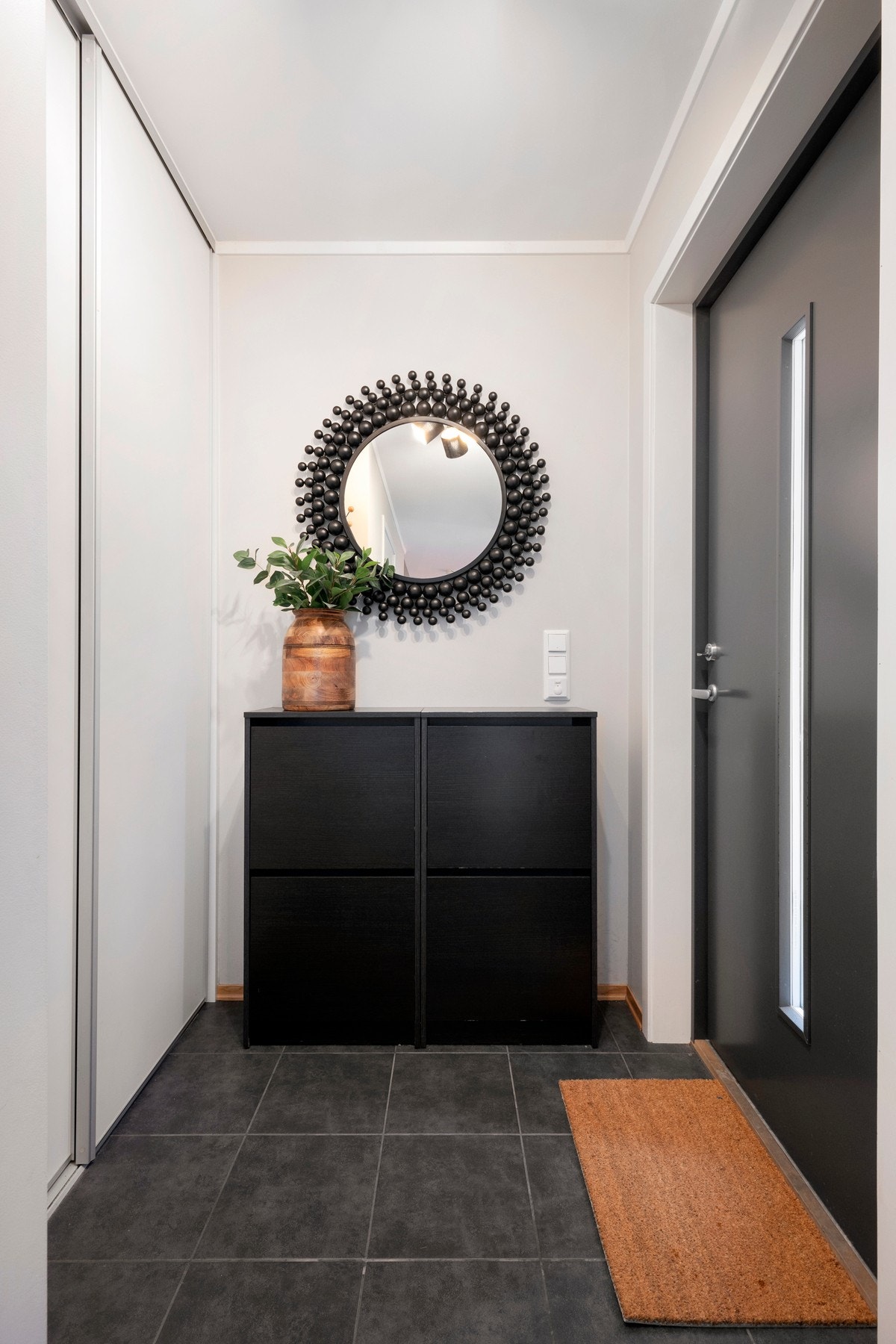 Lys entré med praktiske fliser på gulv og en romslig skyvedørsgarderobe til oppbevaring av yttertøy og sko Galleribilde