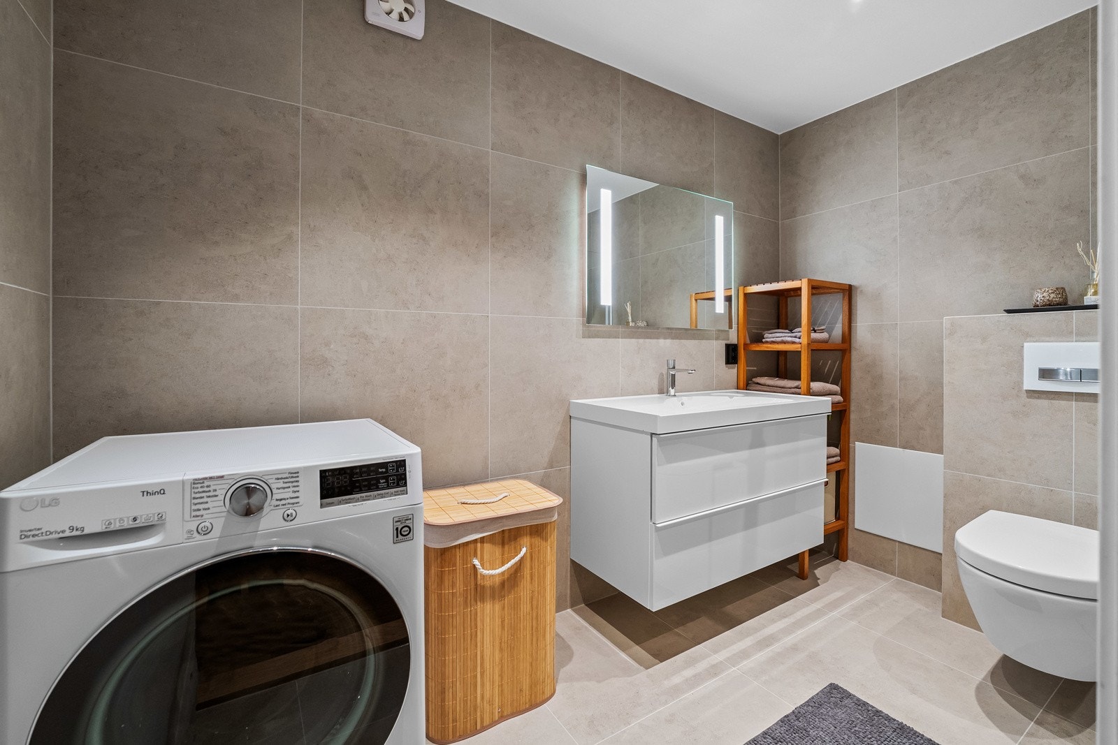 Badet er utstyrt med servant med underskap, veggfestet klosett og et stort speil med integrert belysning. Galleribilde