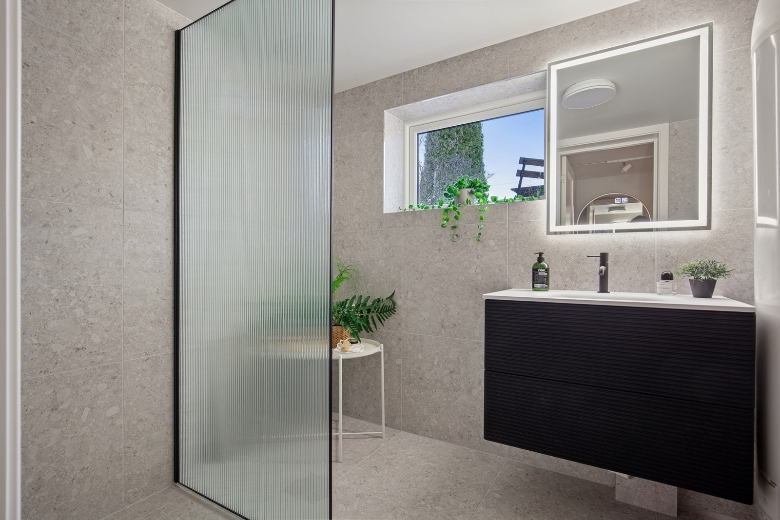 Pent flislagt bad med behagelig gulvvarme, utstyrt med baderomsinnredning og servant, speil, samt dusj med glassvegg. Det er opplegg for vaskemaskin. Galleribilde