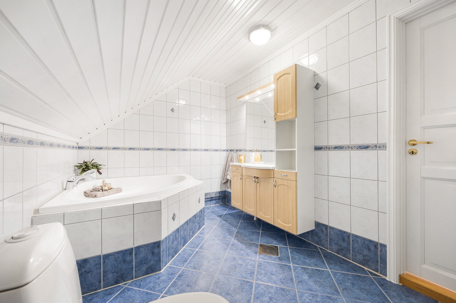 Badet er romslig og har baderomsinnredning med benkeskap og veggskap med profilerte fronter, samt speil over servanten. Rommet er utstyrt med badekar, servant og gulvstående klosett Galleribilde