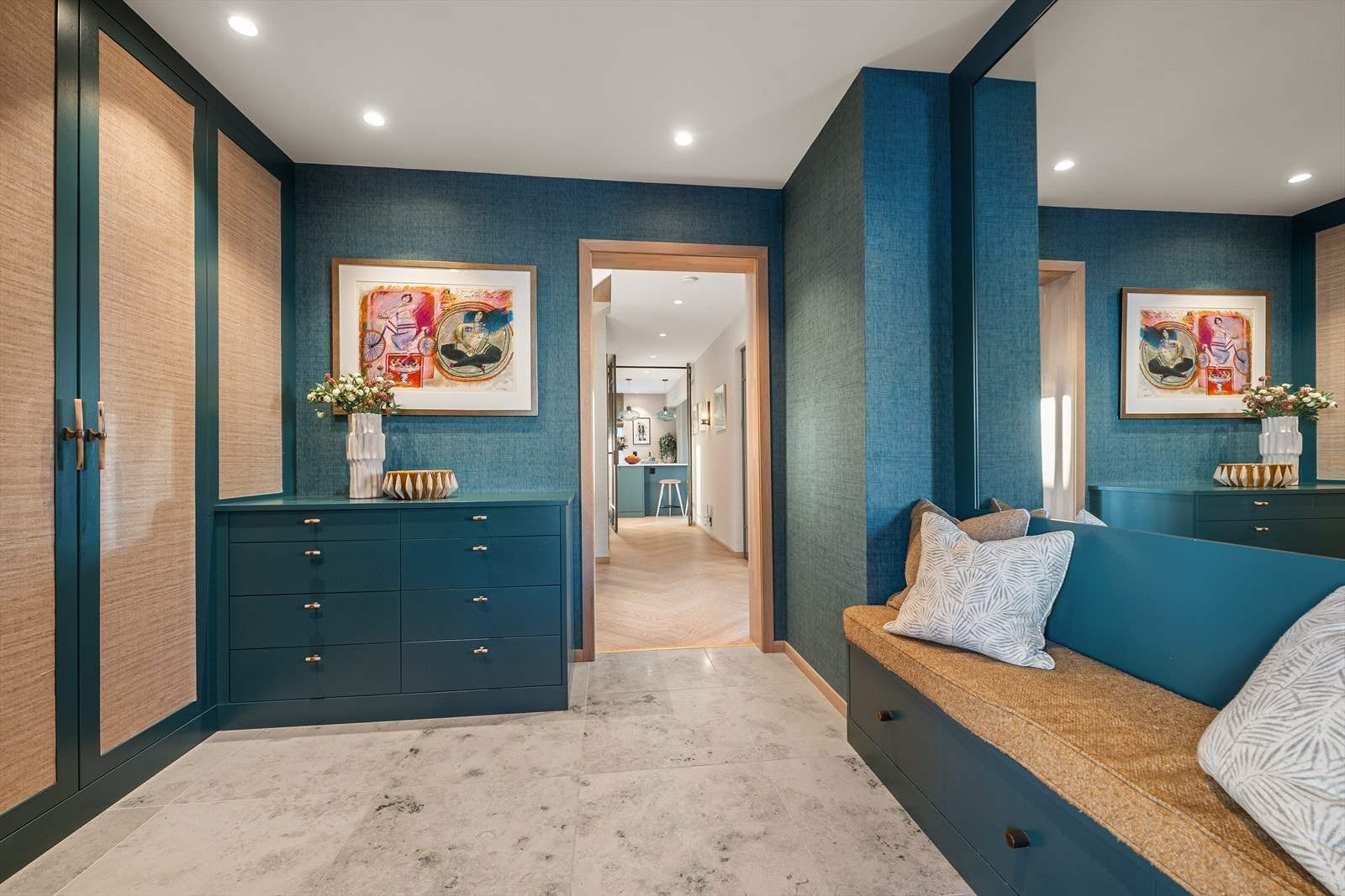 Hallen har plassbygget interiør og garderobeløsning i eik med integrert belysning, levert av Bokhyllespesialisten - Gulvet er belagt med stilrene Jura Grey-fliser fra Sigvartsen med varmekabler, og veggene er dekorert med eksklusiv tapet Galleribilde