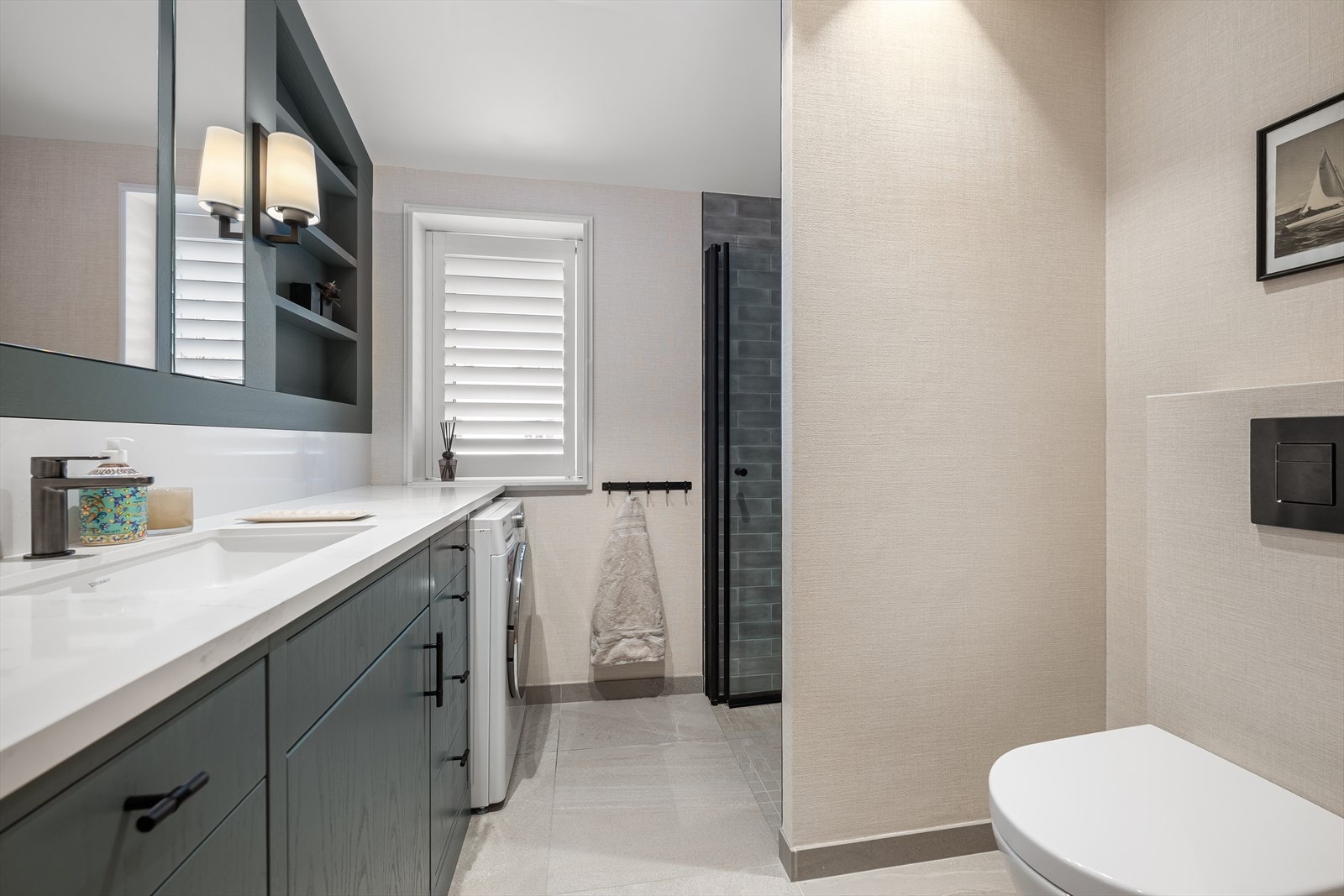 Bad nummer to er tilsvarende stilrent utført med plassbygget interiør i eik fra Bokhyllespesialisten, Silestone benkeplate, dusjnisje med armatur fra Tapwell, toalett, opplegg for vaskemaskin, fliser, eksklusiv baderomstapet, spotbelysning og vindusshutte Galleribilde