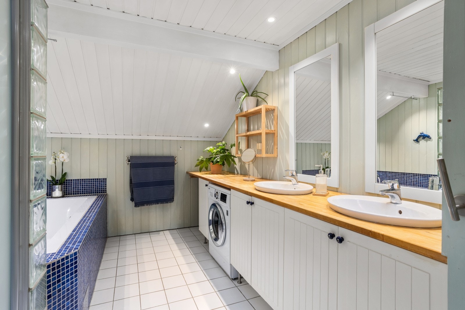 Stort, flislagt bad fra 2006. Det er montert en praktisk arbeidsbenk til klesvasken over nisjen for vaskemaskin. Dobbelt servant med speil på vegg ovenfor Galleribilde