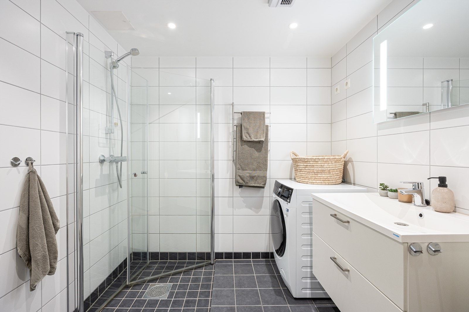 Badet er moderne og pent med downlights i tak, grå fliser på gulv, hvite fliser på veggene og varmekabler i gulvet. Galleribilde