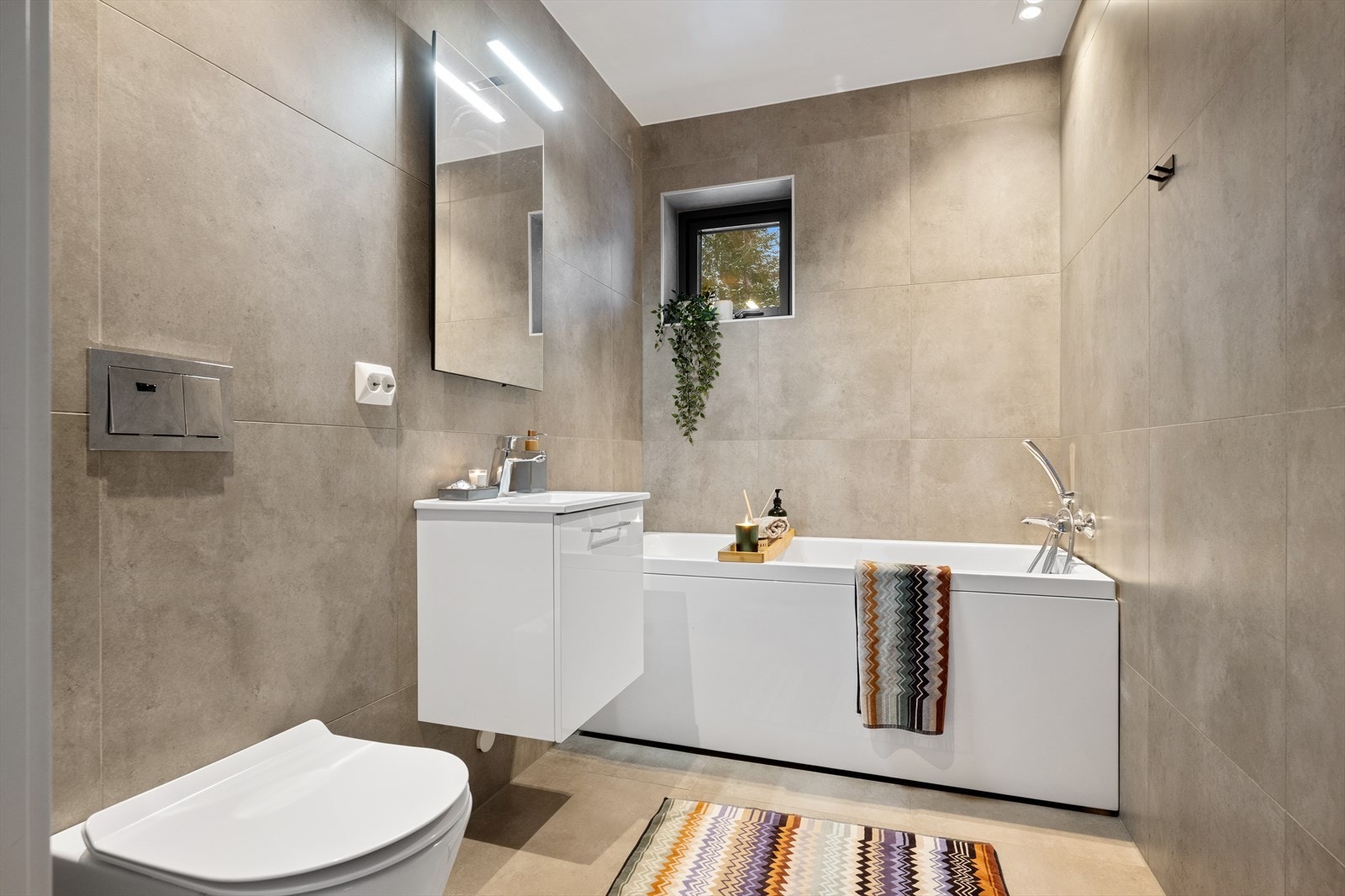 Badet er innredet med servantskap med nedfelt servant, speil med belysning, vegghengt klosett med innebygget sisterne samt badekar, som er godt egnet for barnefamilier. Hvis dusj foretrekkes, kan badekar fjernes og man kan sette opp glassvegg. Galleribilde