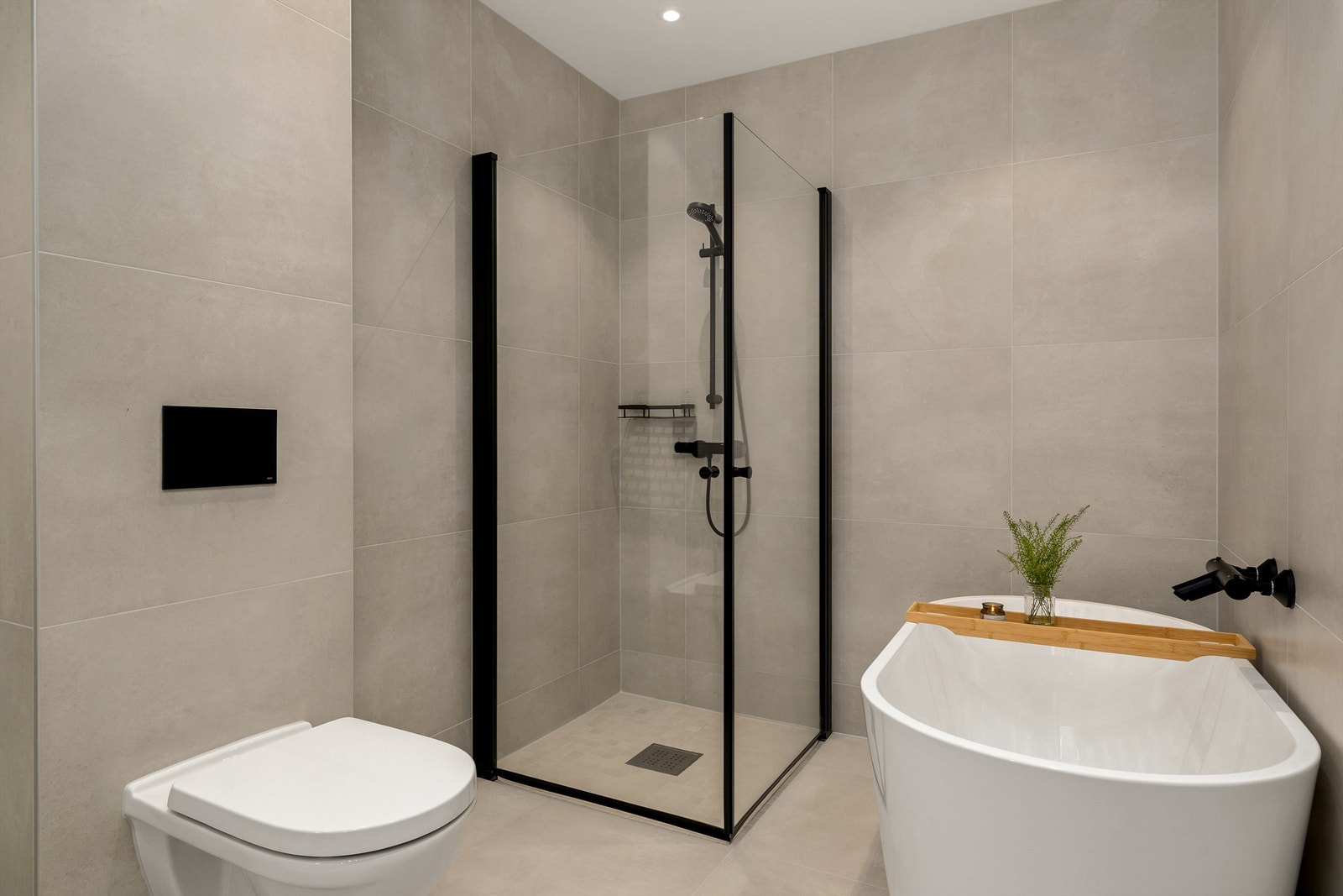 Lekkert flislagt bad med badekar, dusjnisje og vegghengt toalett Galleribilde