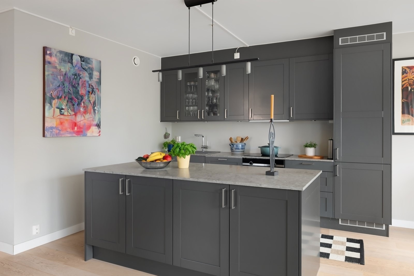 Innredningen er plassert langs én vegg, kombinert med stor kjøkkenøy med rikelig skapinnredning stor arbeidsflate. Galleribilde