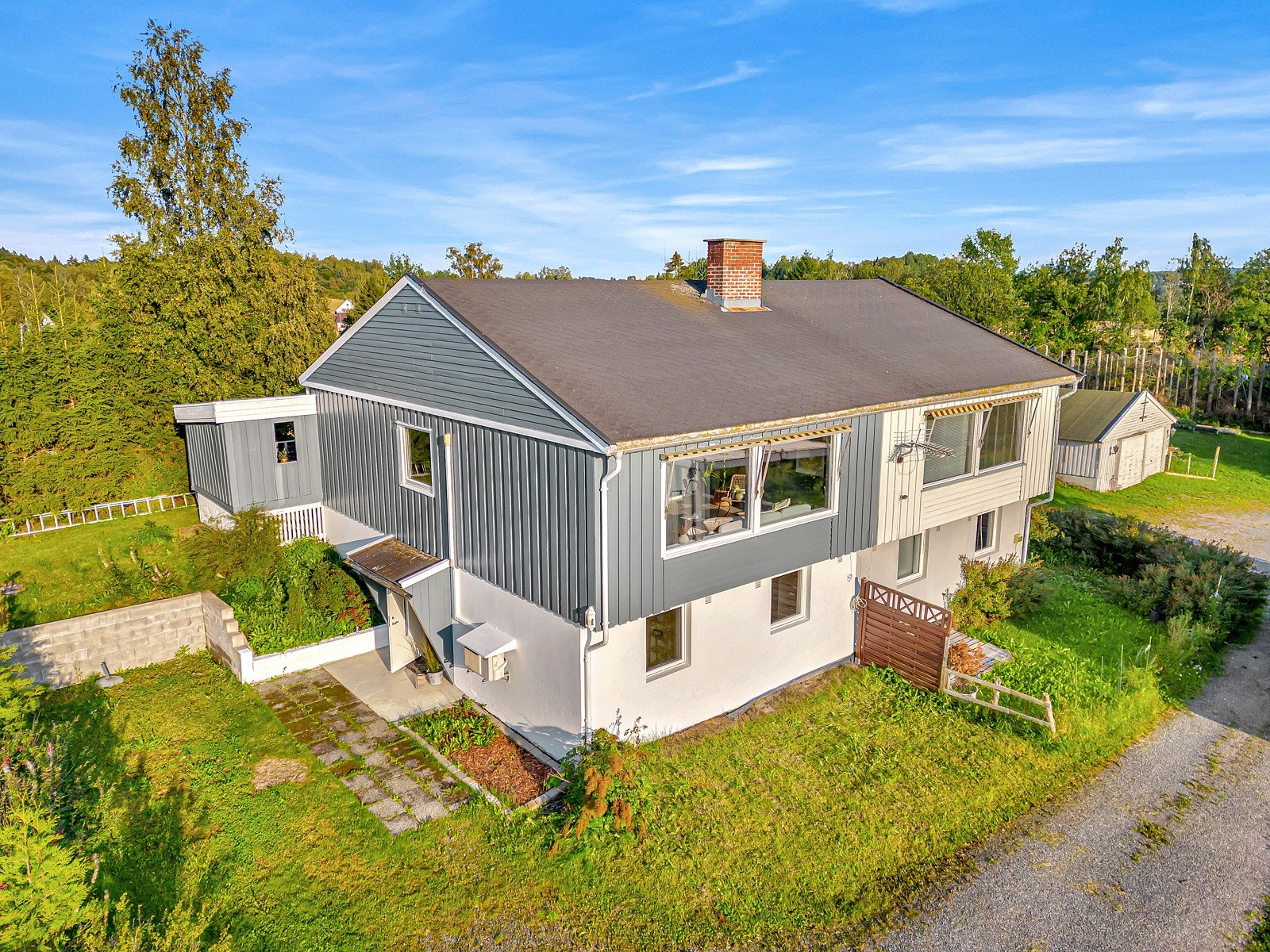 Boligen ligger på en skrånet tomt, opparbeidet med plen og prydbusker. Galleribilde