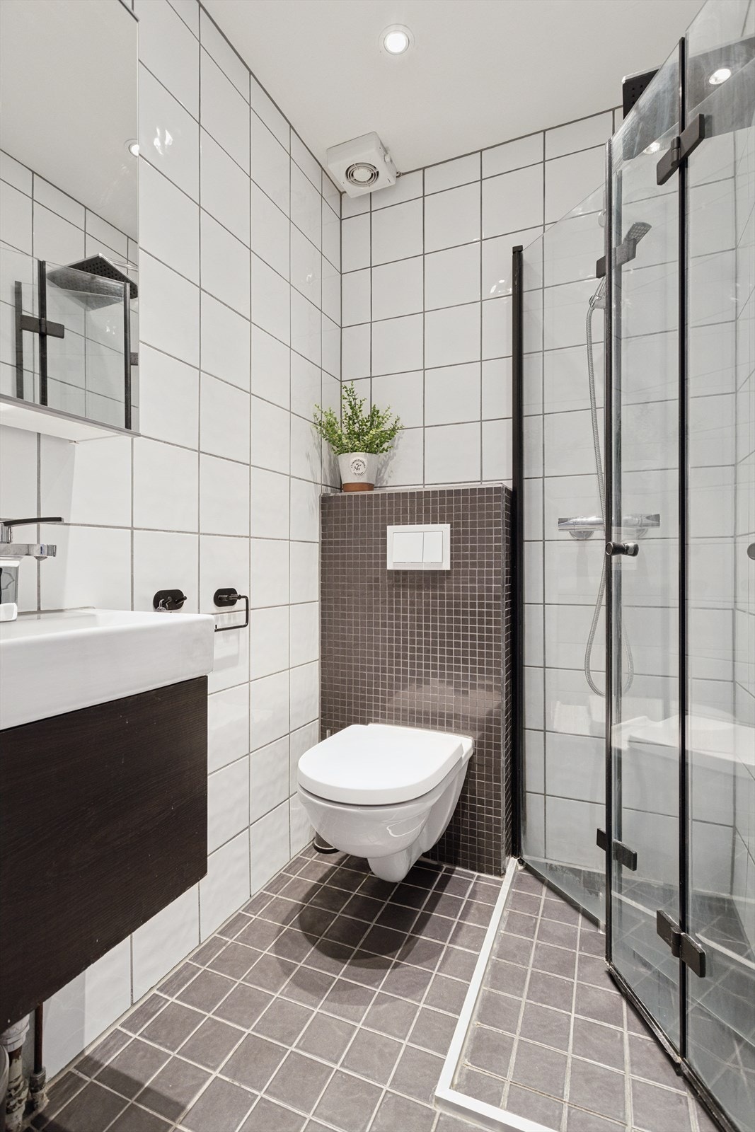 Innredet med veggmontert toalett, dusjhjørne med innsvingbare dører for maskimal utnyttelse av rommet, innredning med nedfelt servant og overhengt speilskap. Galleribilde