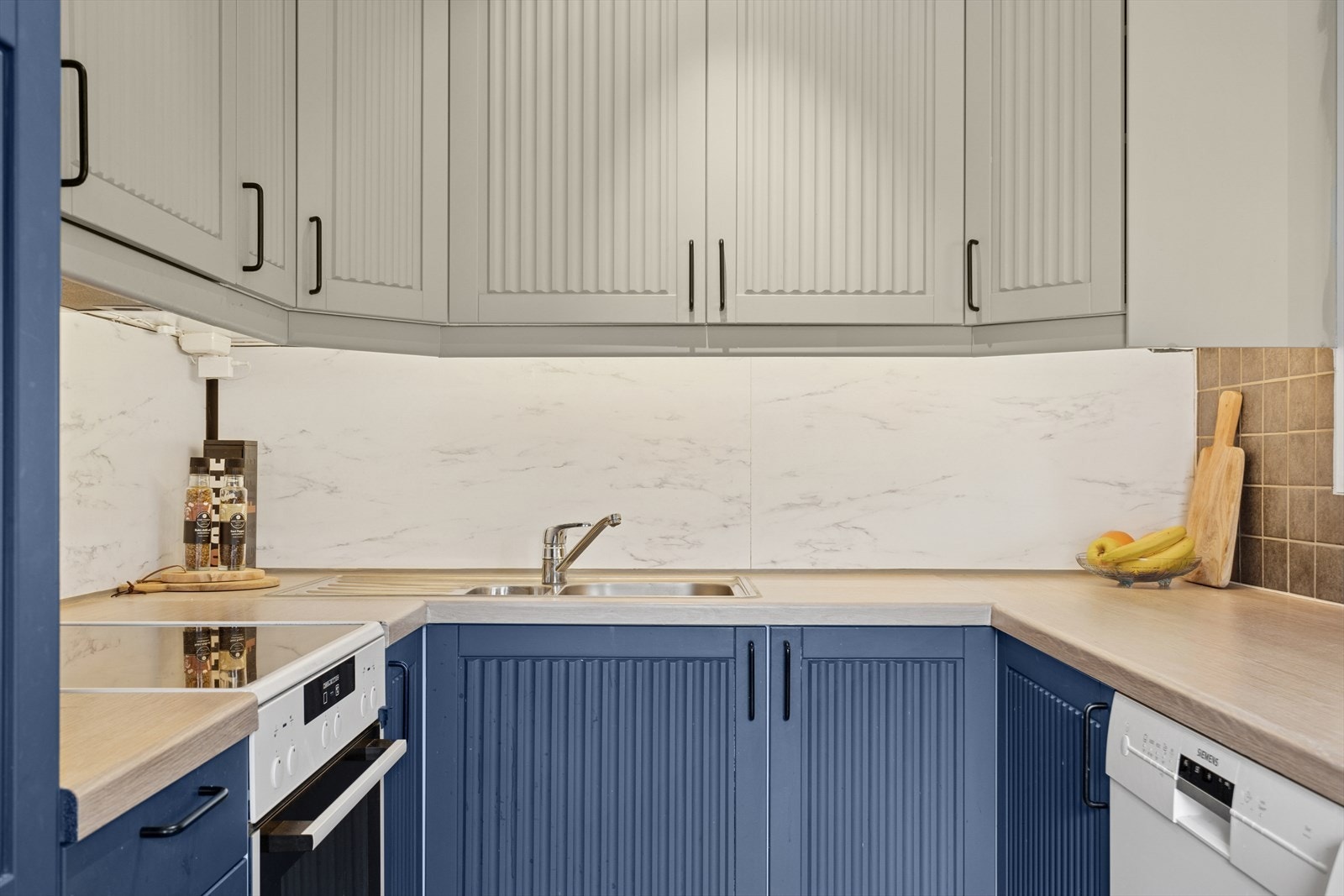 Kjøkkeninnredning med folierte skrog, slette fronter, laminert benkeplate og delikate flis på vegg over benkeplate. Galleribilde