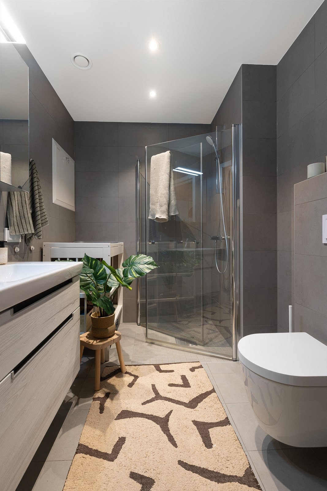 Dempede, eksklusive fargetoner på fliser. Servantskap og speilskap med oppbevaring og lys gir god plass til bleielageret. Galleribilde