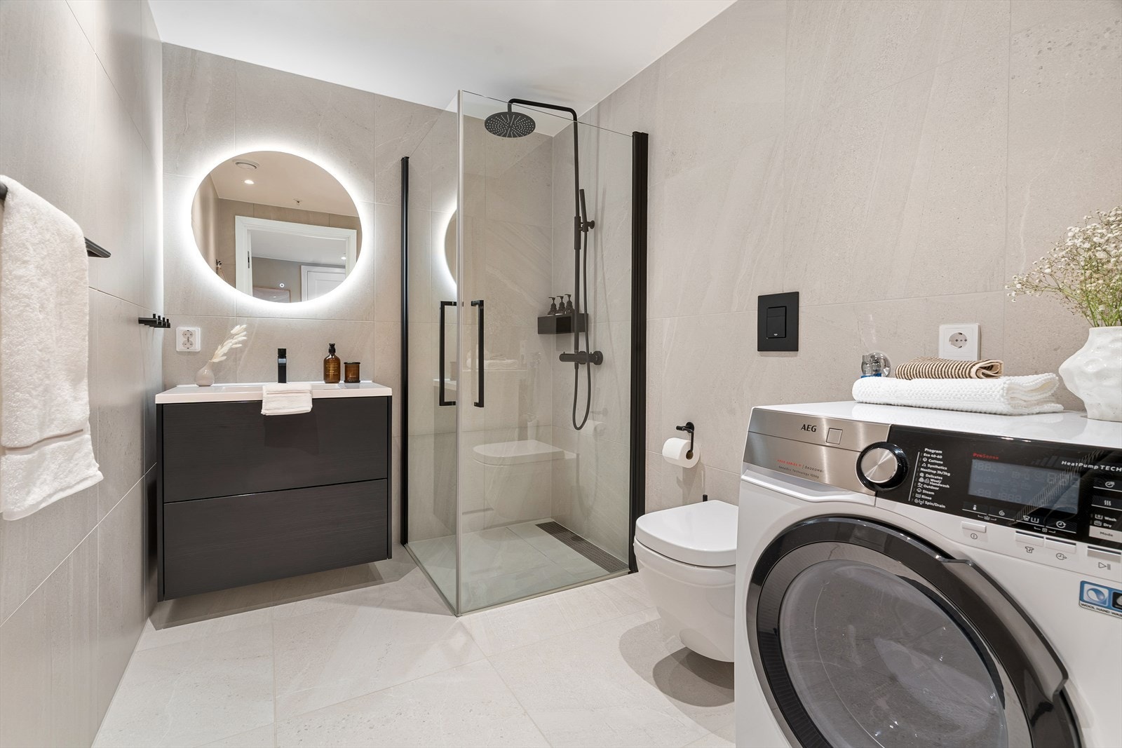 Lekkert og moderne bad med stilrene fliser. Leiligheten er påkostet med gjennomførte detaljer og høy kvalitet. Badet har vegghengt toalett, regnfallsdusj, fastmontert såpehylle, stort speil med lys og romslig innredning fra Drømmekjøkkenet. Galleribilde