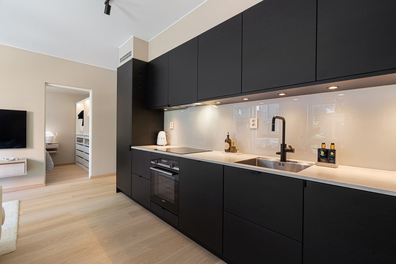 Godt belyst kjøkken med spotter under overskapene, stilren glassplate, gode arbeidsflater og rikelig oppbevaringsplass. Galleribilde