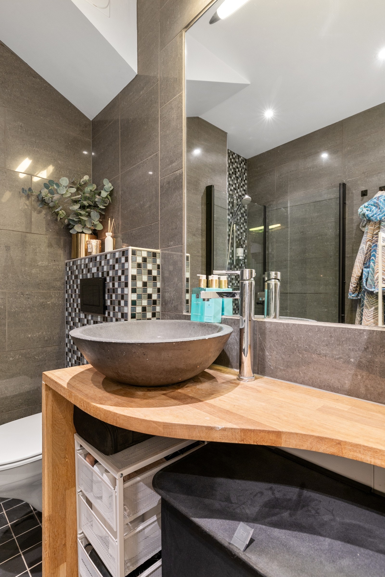 Rommet har nytt dusjhjørne med glassdører (2025), vegghengt toalett, innredning med bollevask og speil, samt opplegg for vaskemaskin. Galleribilde