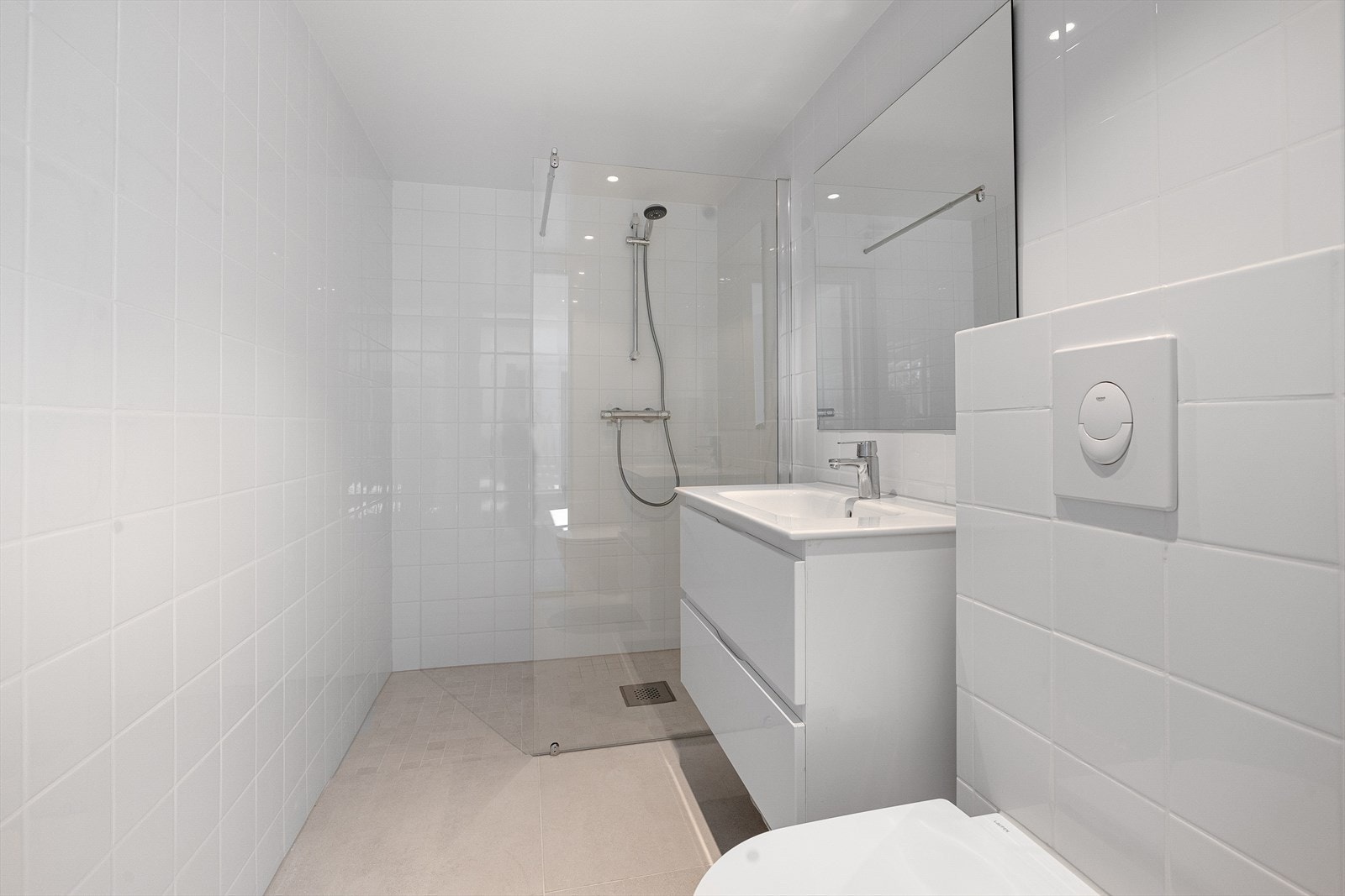 Lyst og pent bad, med delikate fliser på vegger og gulv. Badet er innredet med servant i innredning med skuffer og speil på vegg. Dusjhjørne med hånddusj og glassdør. Vegghengt toalett Galleribilde