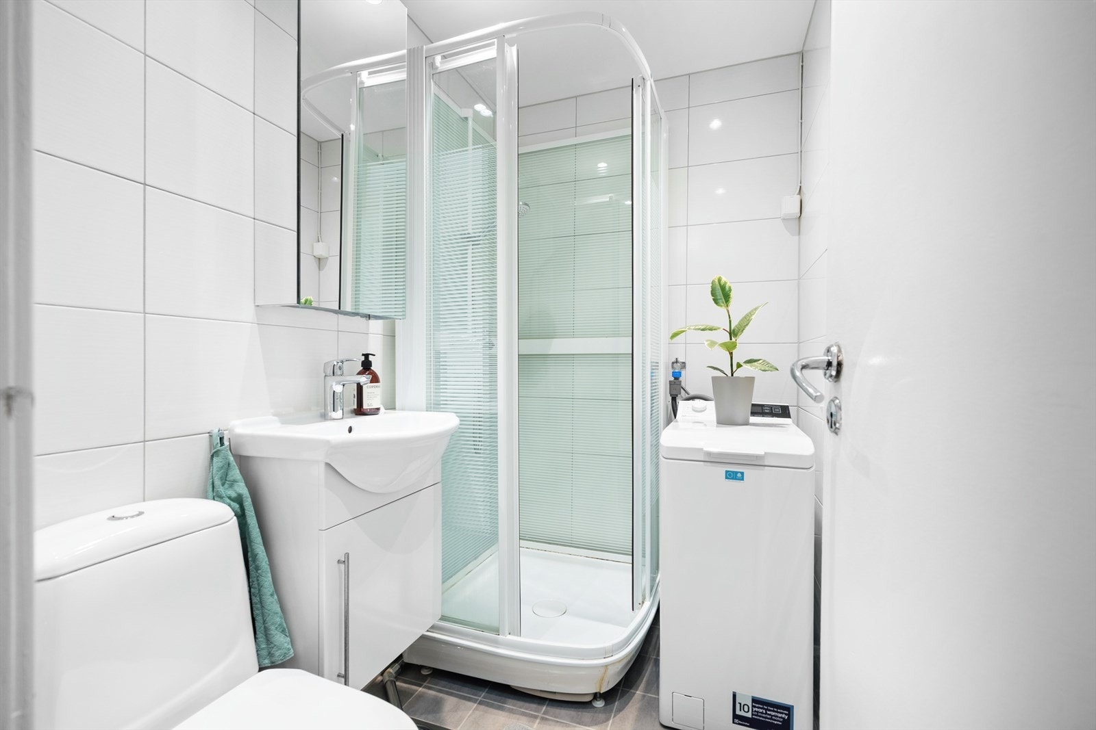 Lyst og funksjonelt bad med dusjkabinett og opplegg for vaskemaskin. Galleribilde