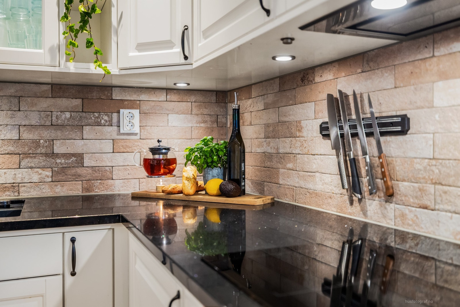 Flislagte felt på vegg over benkeplater av stein og lysarmaturer under overskap Galleribilde