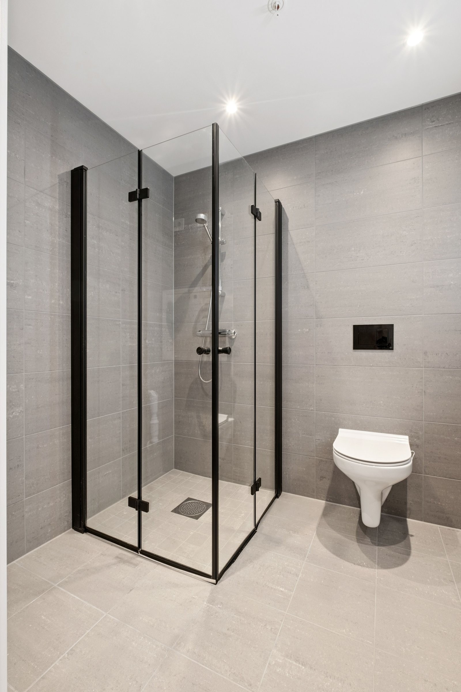 Praktisk dusj løsning med sorte glassdører som kan foldes - gir både et stilrent utrykk og fleksibel plassutnyttelse. God plass til både vaskemaskin og tørketrommel. Galleribilde