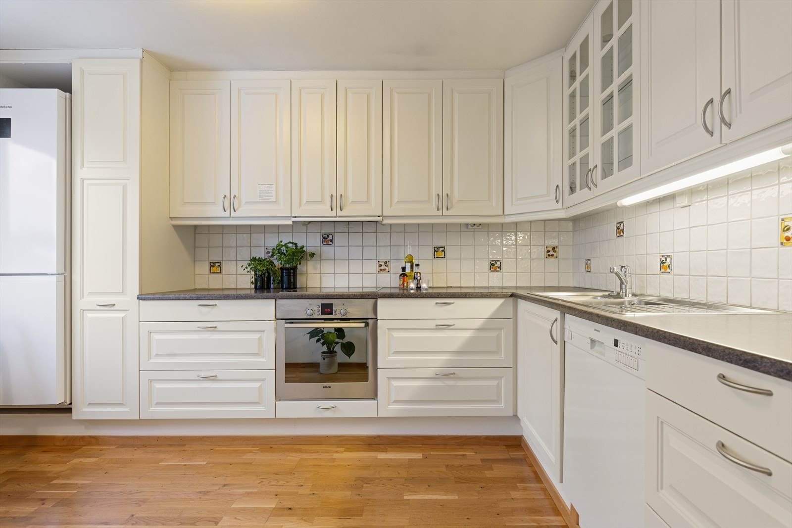 Stort og lyst kjøkken med profilerte fronter og laminat benkeplate med fliser over benken Galleribilde