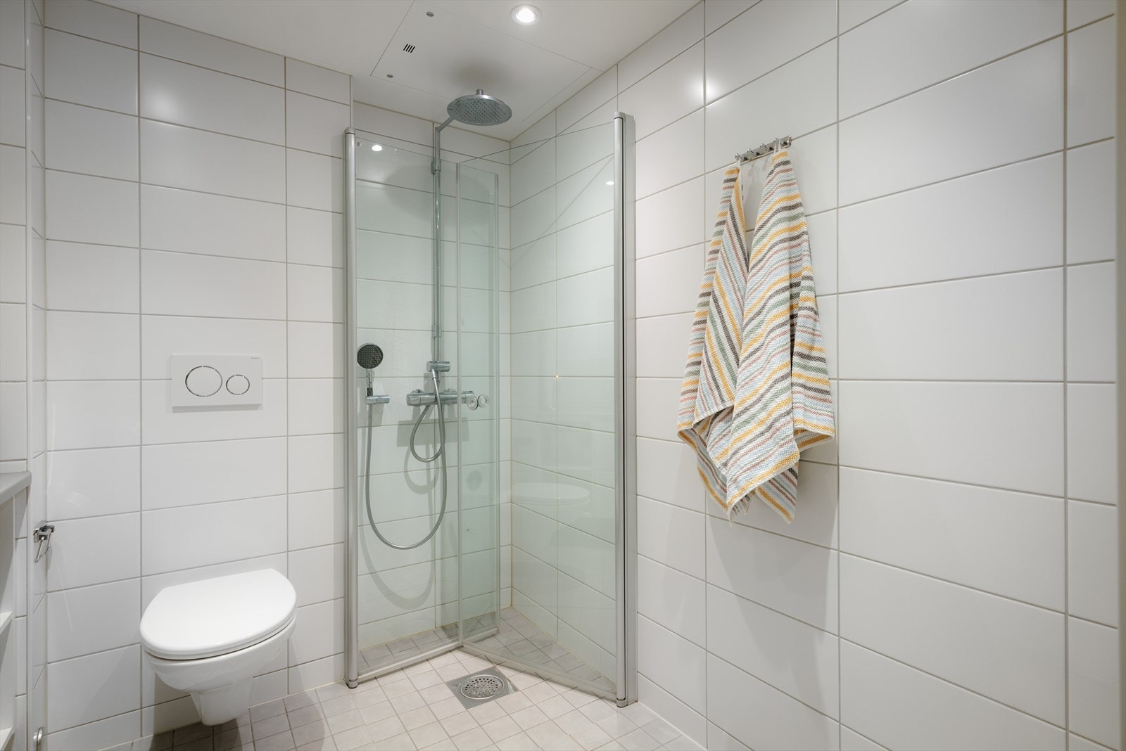 Dusjhjørne med svingbare dører i glass og vegghengt toalett. Galleribilde