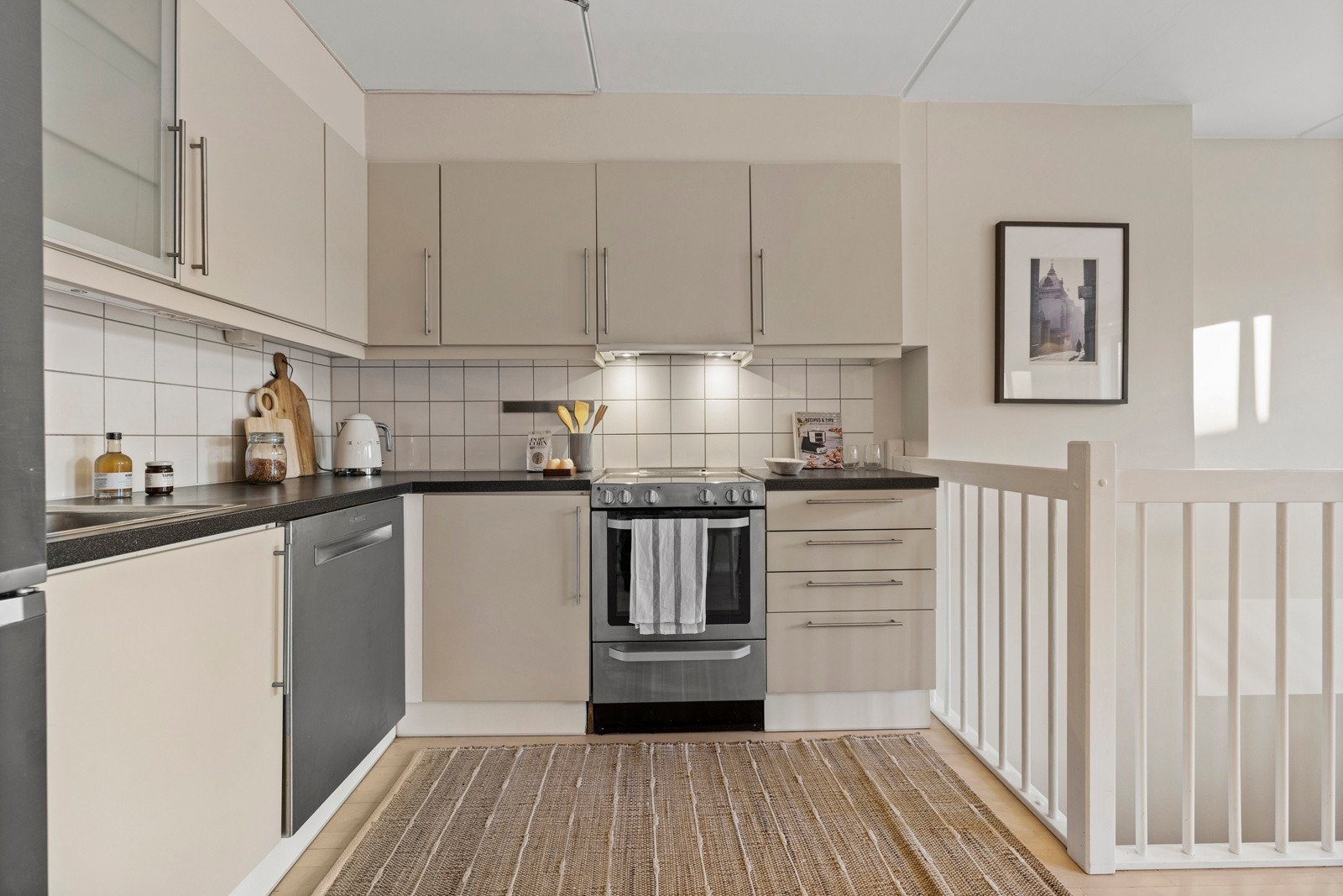 Kjøkkeninnredning med slette fronter, stålhåndtak, overskap og fliser på vegger Galleribilde