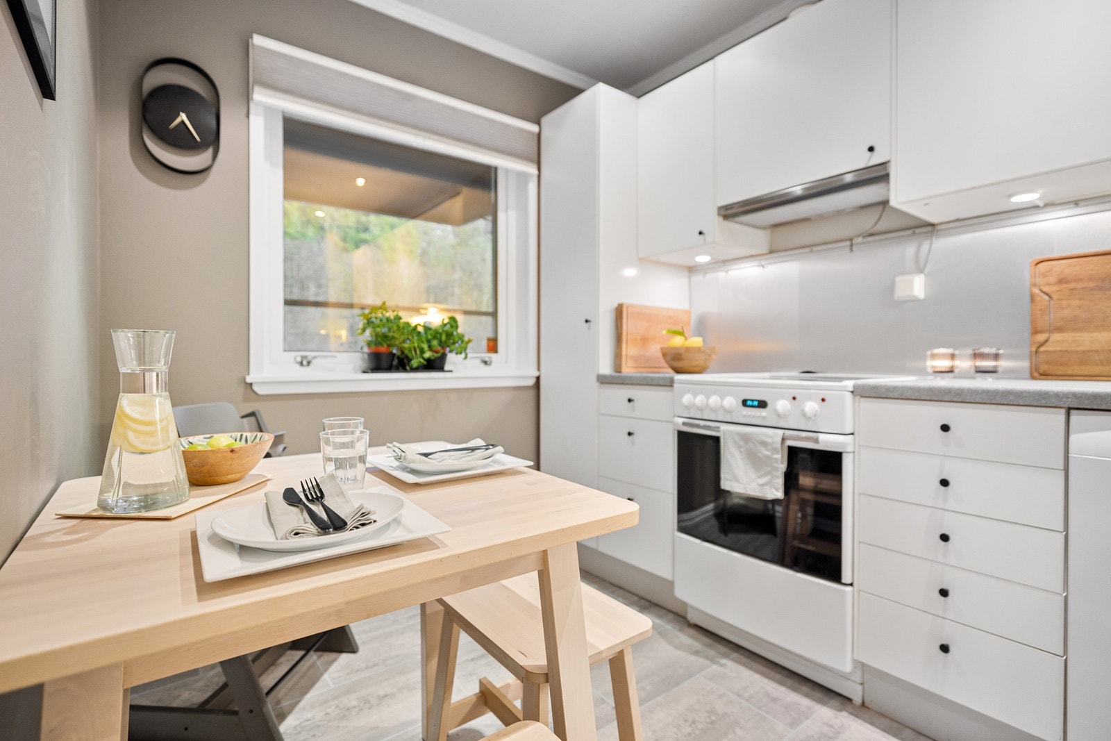 Fra entrè føres en videre til boligens kjøkken. Kjøkkenet har innredning i hvit slett utførelse med lys grå laminat benkeplate med platekledning over, samt belysning over kjøkkenbenk Galleribilde