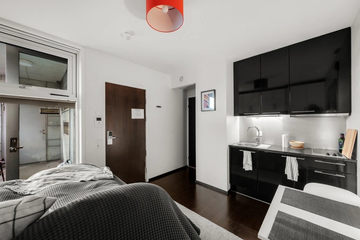 Kjøkkeninnredning med svarte fronter, stålplate og belysning over benkeplate i stein og oppvaskkum. Videre utstyrt med kjøleskap m/ fryseboks og 2-soners koketopp. Galleribilde